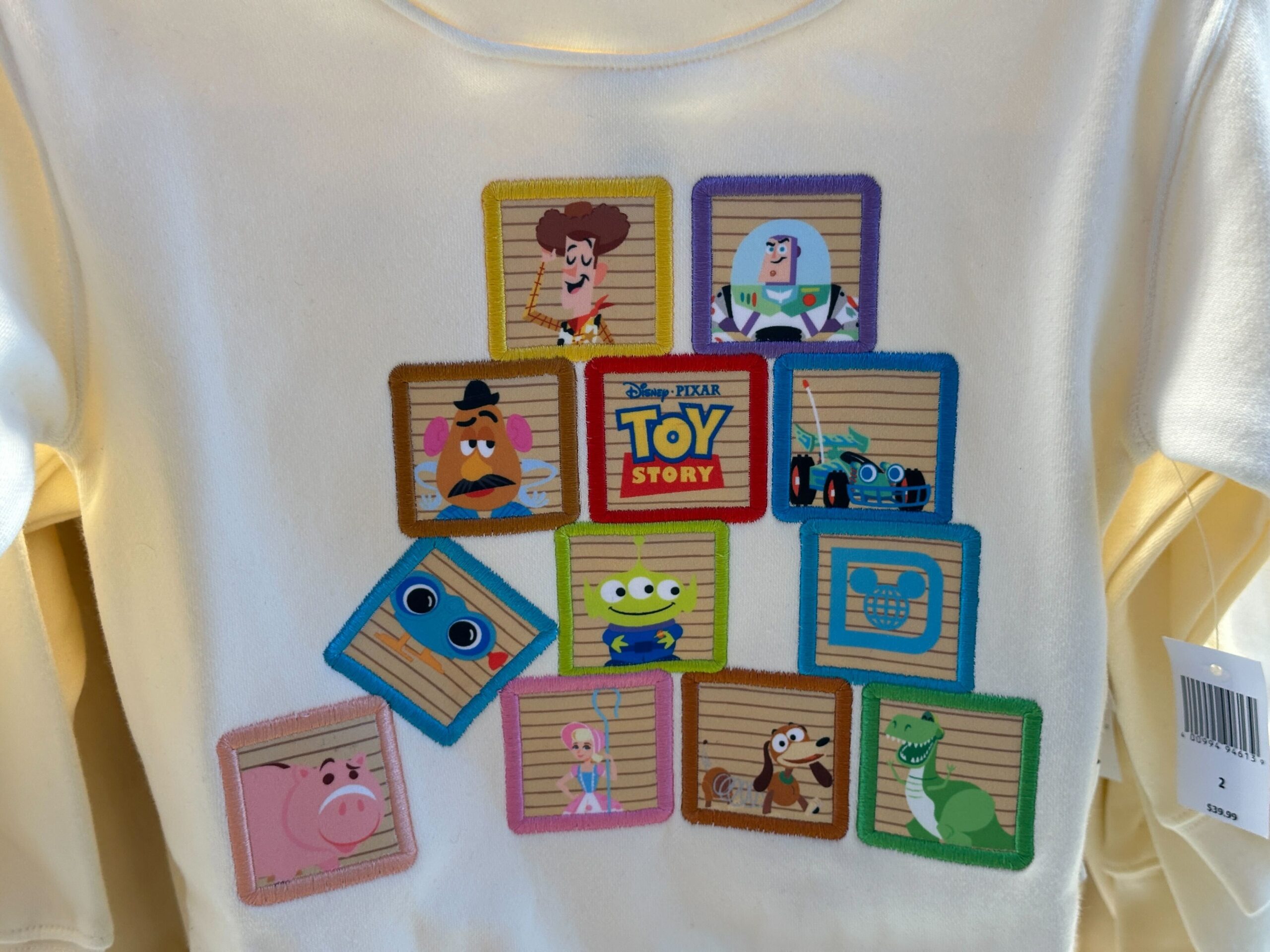White shirt with bright squares of Toy Story characters, marking 30 years—similar to shirts at Disney Parks, no castle pictured.