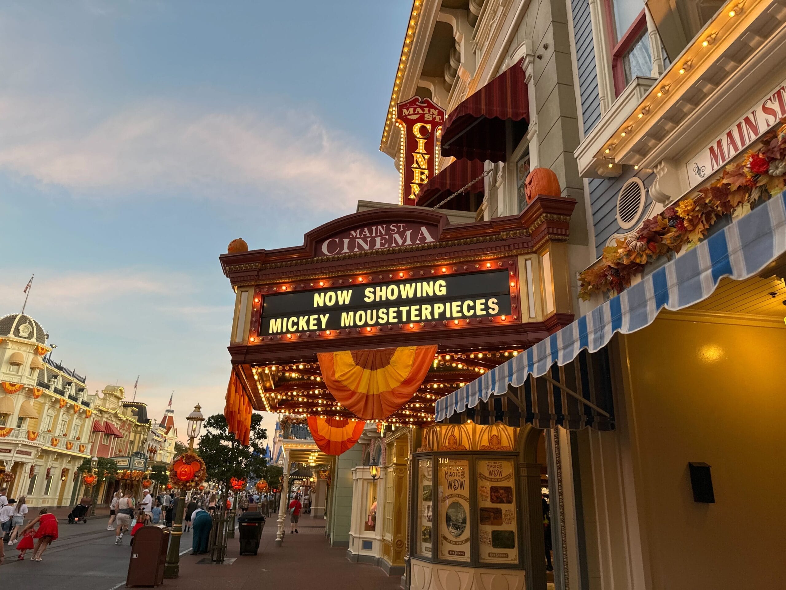 Main Street Cinema marquee aglow, displays “Now Showing Mickey Mouseterpieces,” with festive decor outside, Main Street U.S.A. style.