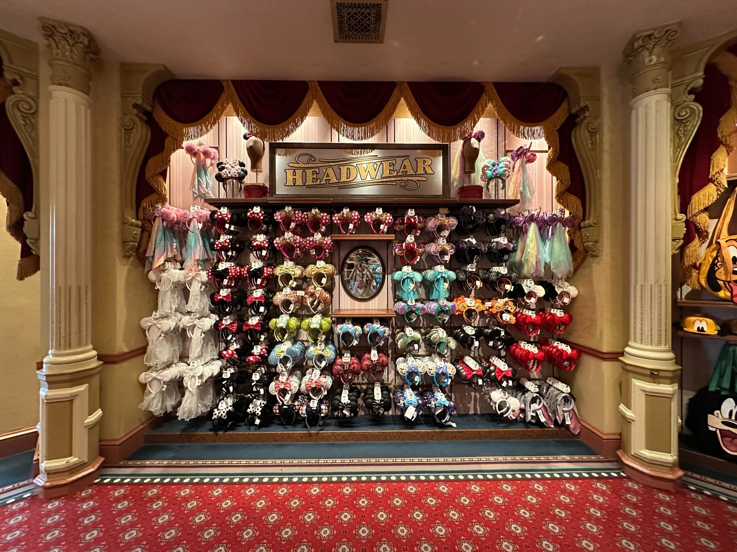 Shelves of iconic Disney Ear Headbands and hats in a red-carpeted Disney World shop, merchandise prices clearly displayed.