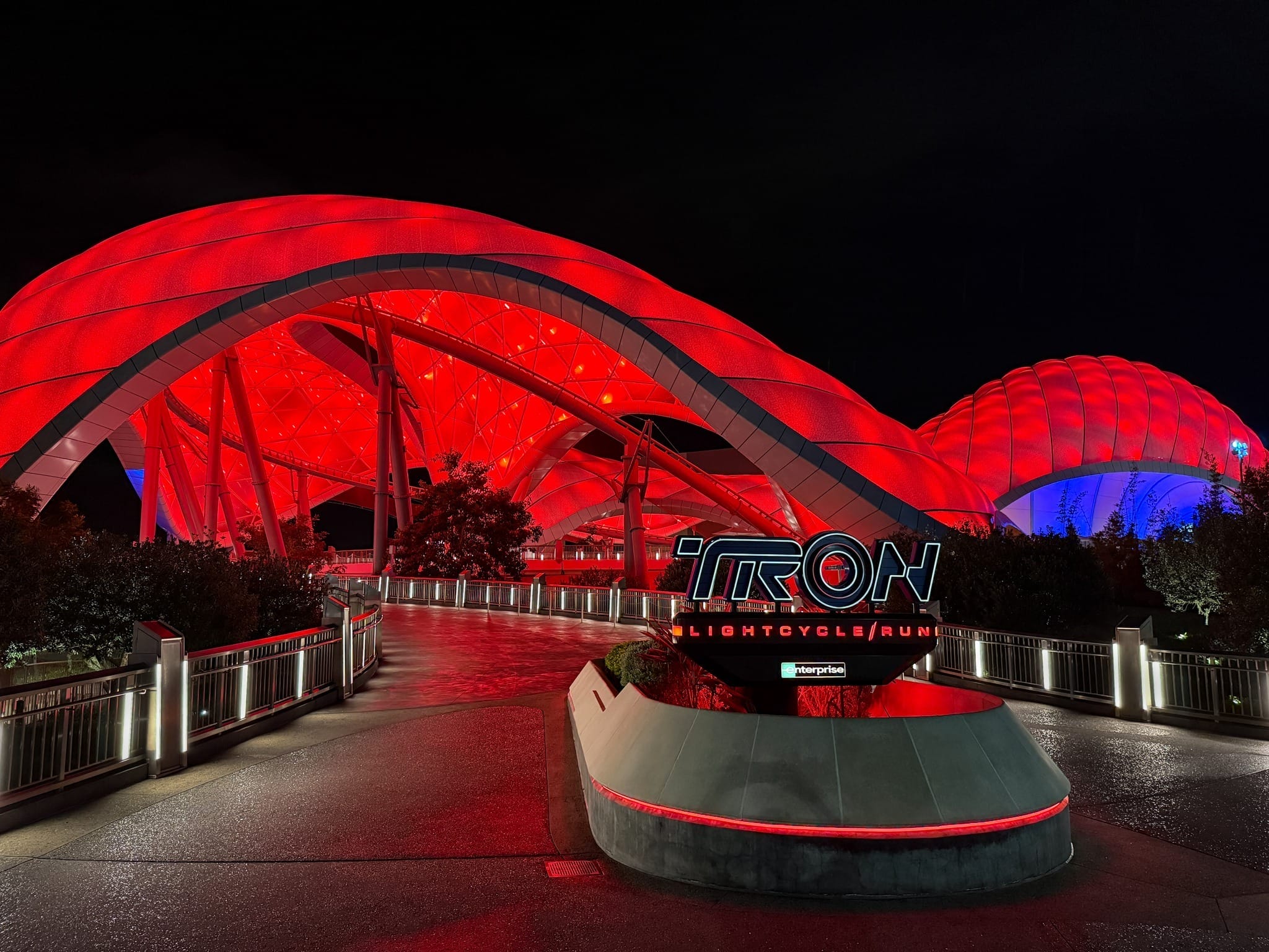 The TRON Lightcycle/Run entrance glows red at night with a futuristic canopy, rivaling nighttime vibes of other Disney parks rides.