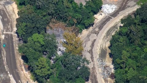 Aerial photo of Tom Sawyer Island at Disney, wooded with debris piles and construction materials by a curved path—no castle visible.