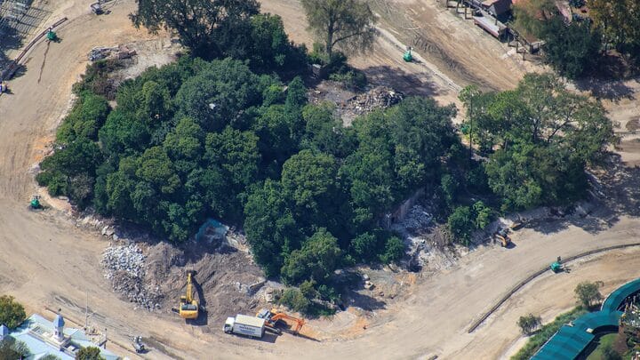 Aerial view of Tom Sawyer Island in a Disney park, trees clustered amid demolition and construction vehicles, no castle visible.