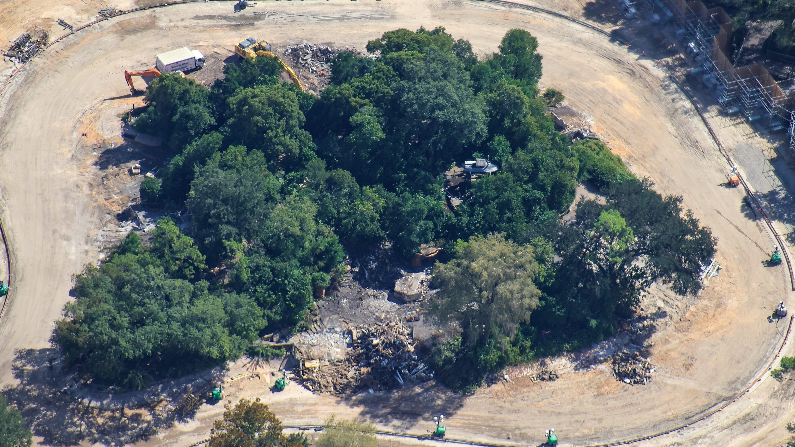 Aerial view of Tom Sawyer Island at a Disney park shows a circular construction site with trees and debris, no castle in sight.