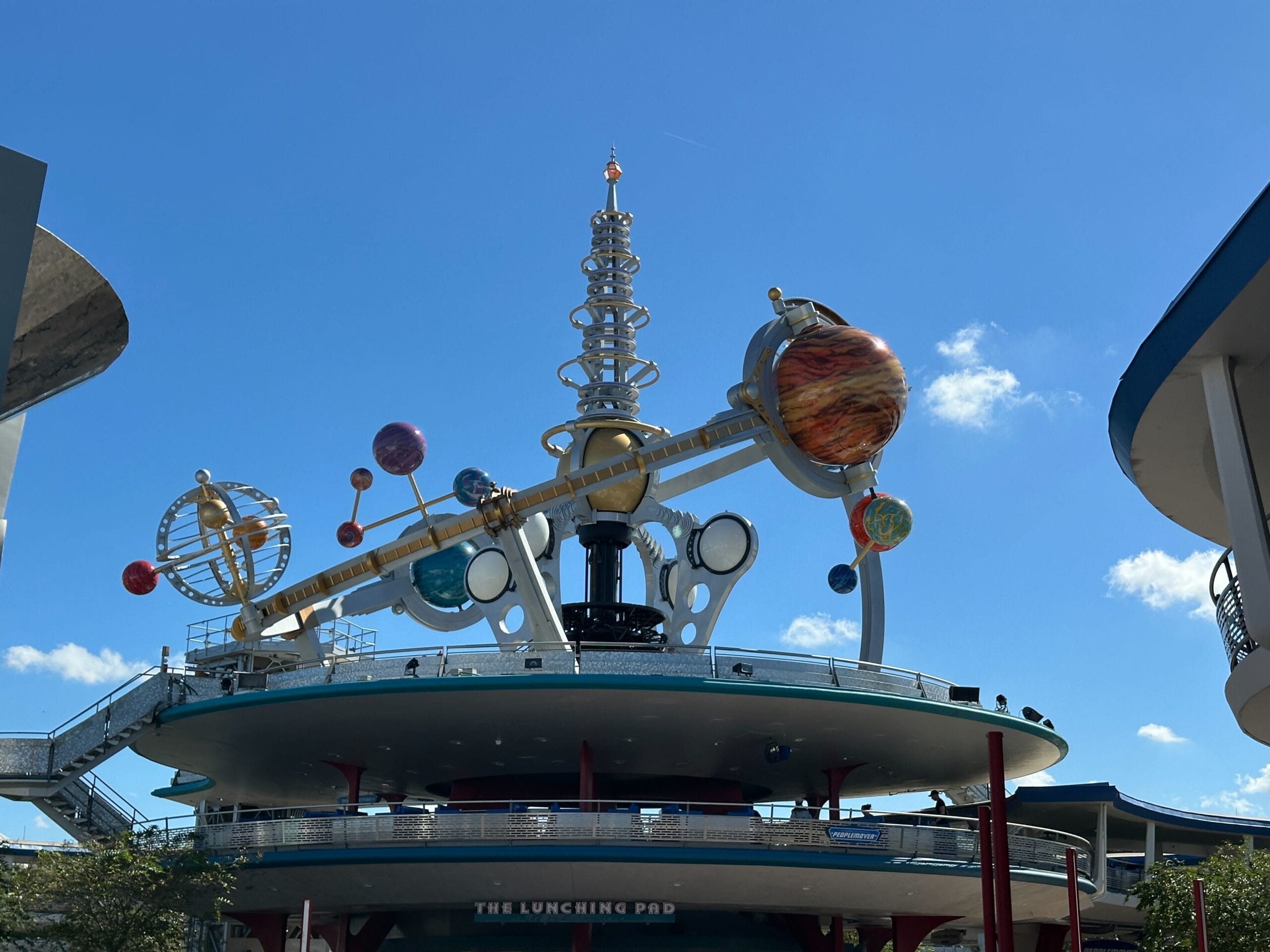 Astro Orbiter ride spins with vibrant planets and rings, echoing Tomorrowland’s sleek Disney parks style under a blue sky.