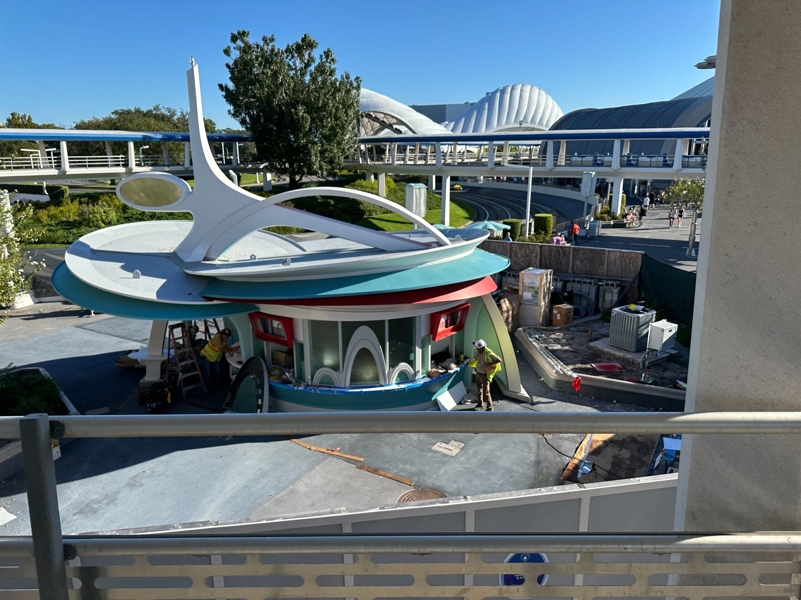A retro-futuristic kiosk under construction at a Disney park, surrounded by lush landscaping and paths, from today's Daily Recap.