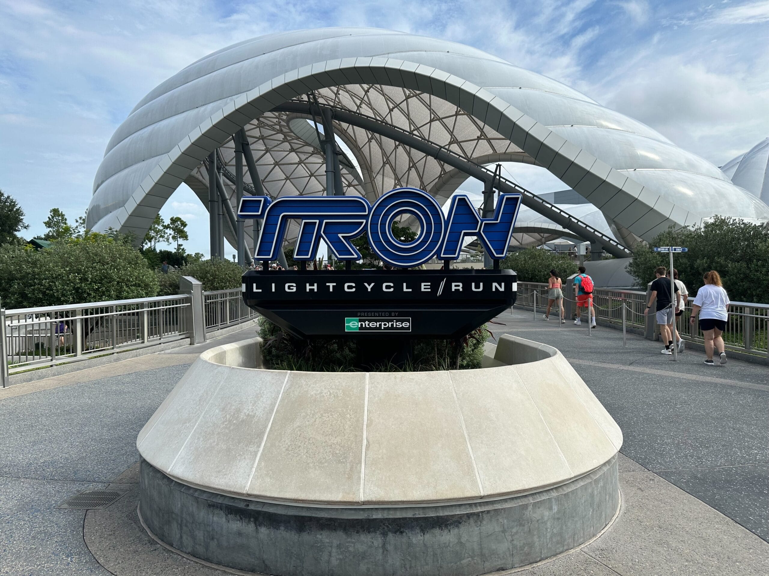 TRON Lightcycle Run sign in front of a sleek, glowing dome, echoing Tomorrowland’s energy at Disney Parks, similar to TRON: Ares.