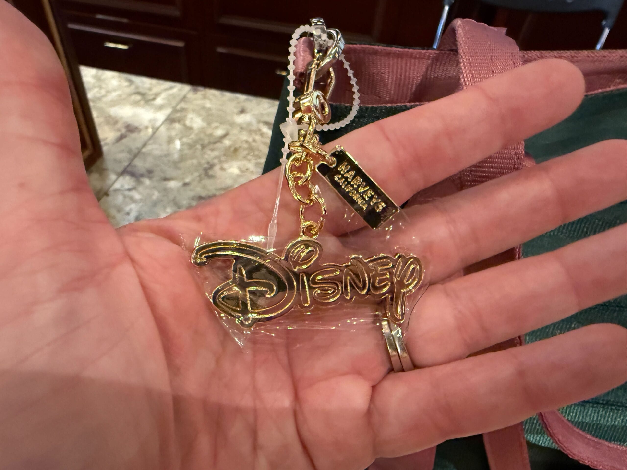 A hand displays a gold Disney keychain over a green Harvey Handbag