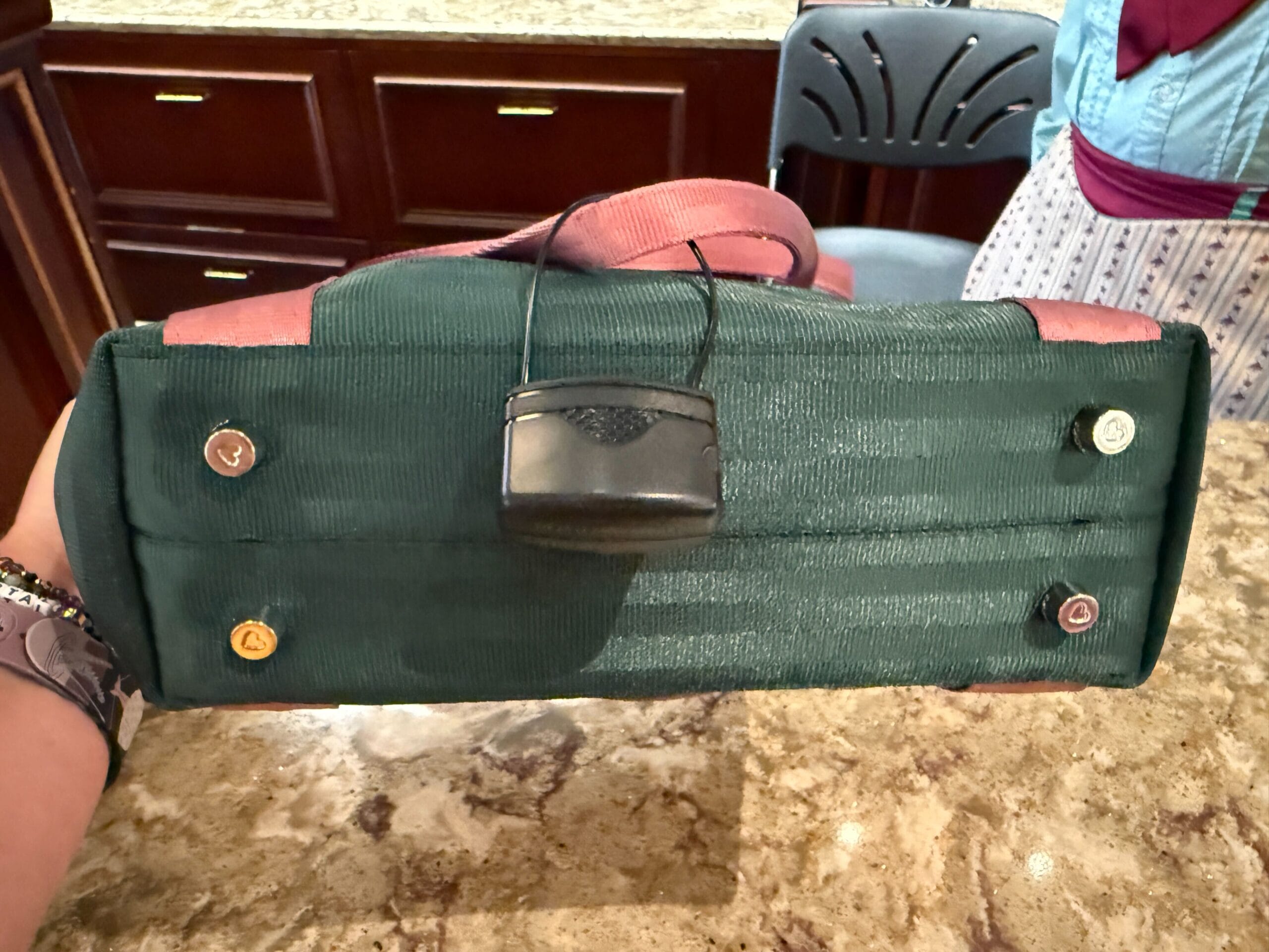 The bottom of a green and pink Harvey Handbag with buttons and a black sensor