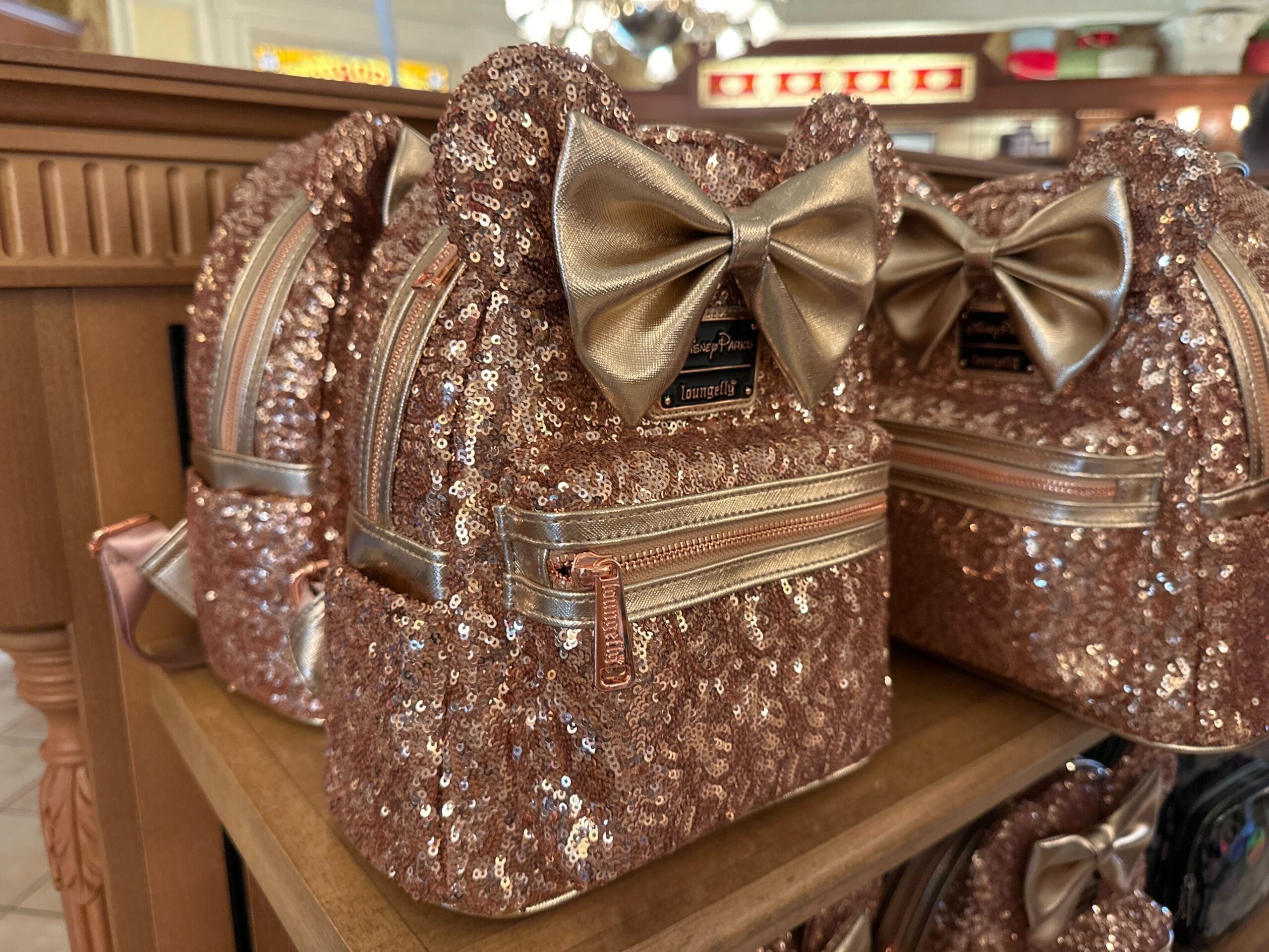 Rose gold sequin backpacks and metallic-bowed Ear Headbands line a wooden shelf in Disney World, home to Cinderella Castle.