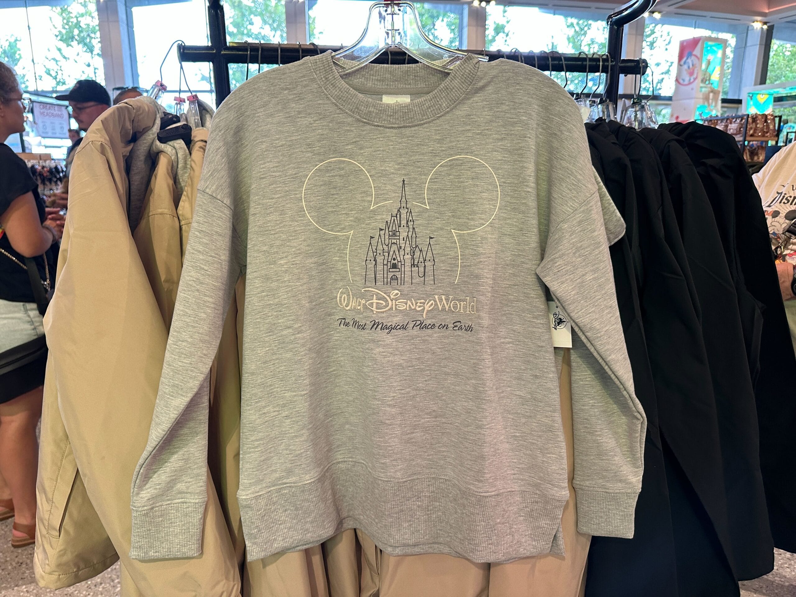 Gray Walt Disney World sweatshirt with an outlined Cinderella Castle—distinct from Disneyland’s Sleeping Beauty Castle—hanging on a rack.