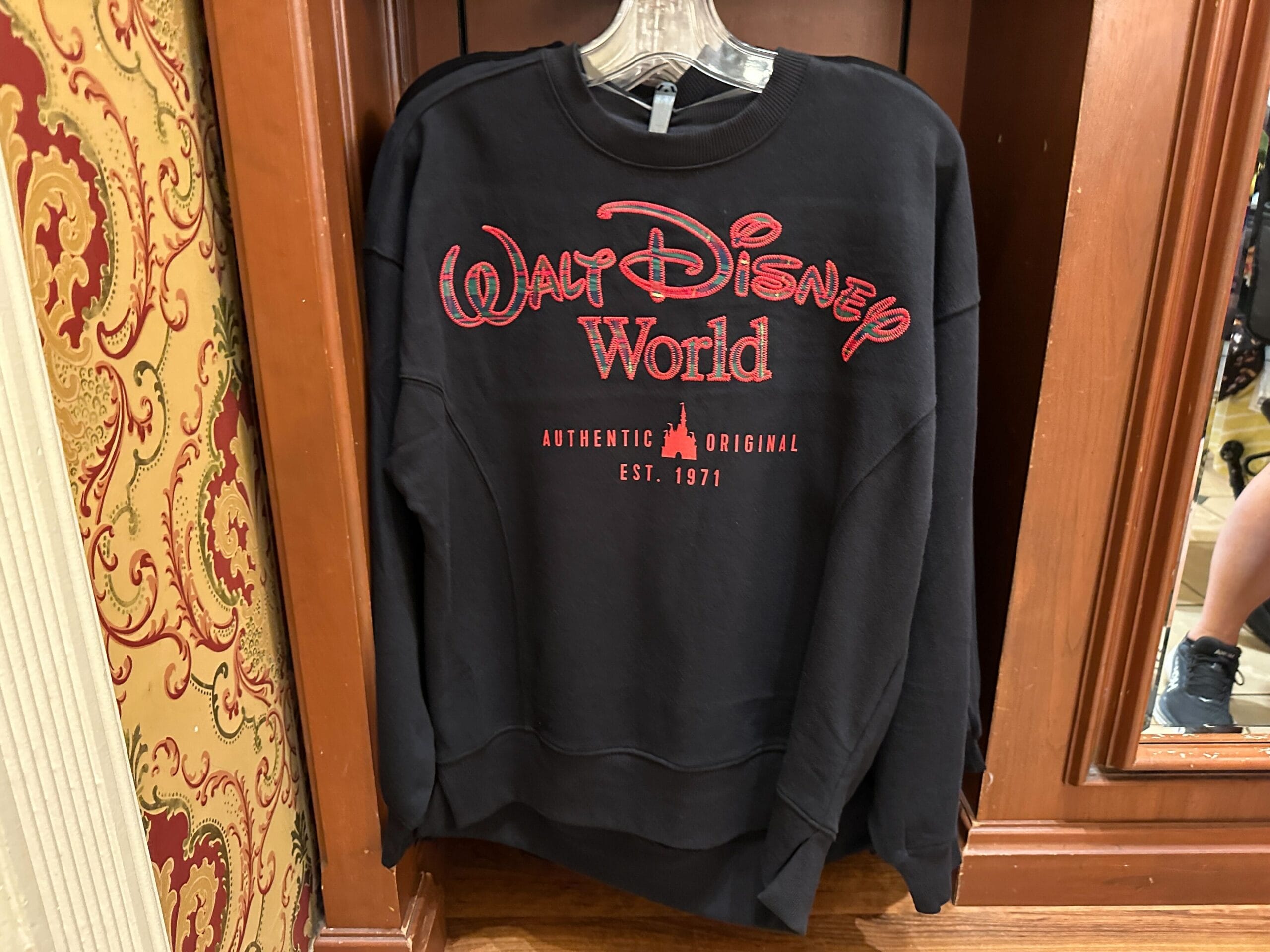 Black "Walt Disney World" sweatshirt with red lettering, displayed on a wooden rack in a festive store, reminiscent of park shops.