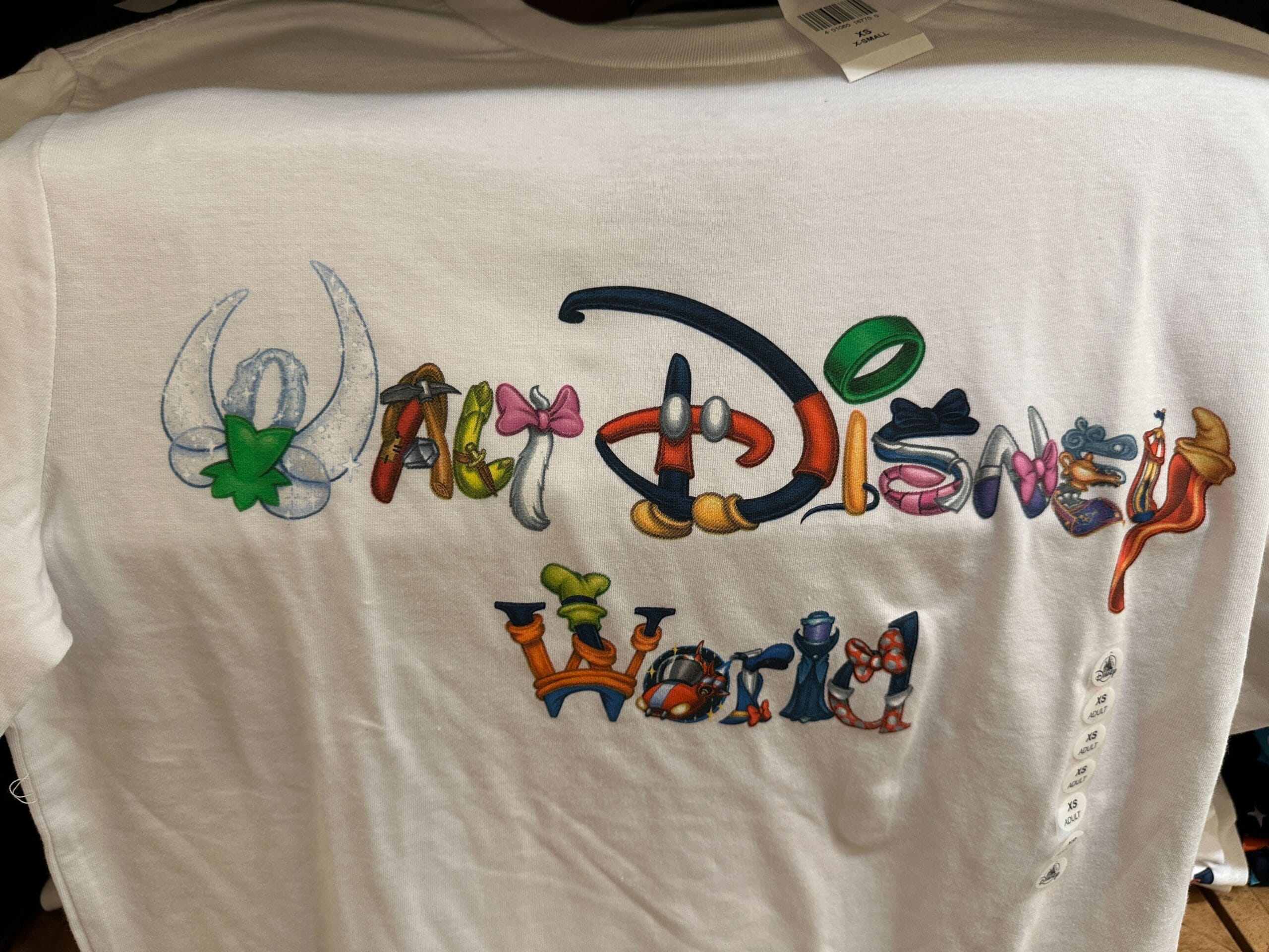 White shirt featuring "Walt Disney World" in vibrant Disney character-themed letters, reminiscent of park merchandise at WDW.