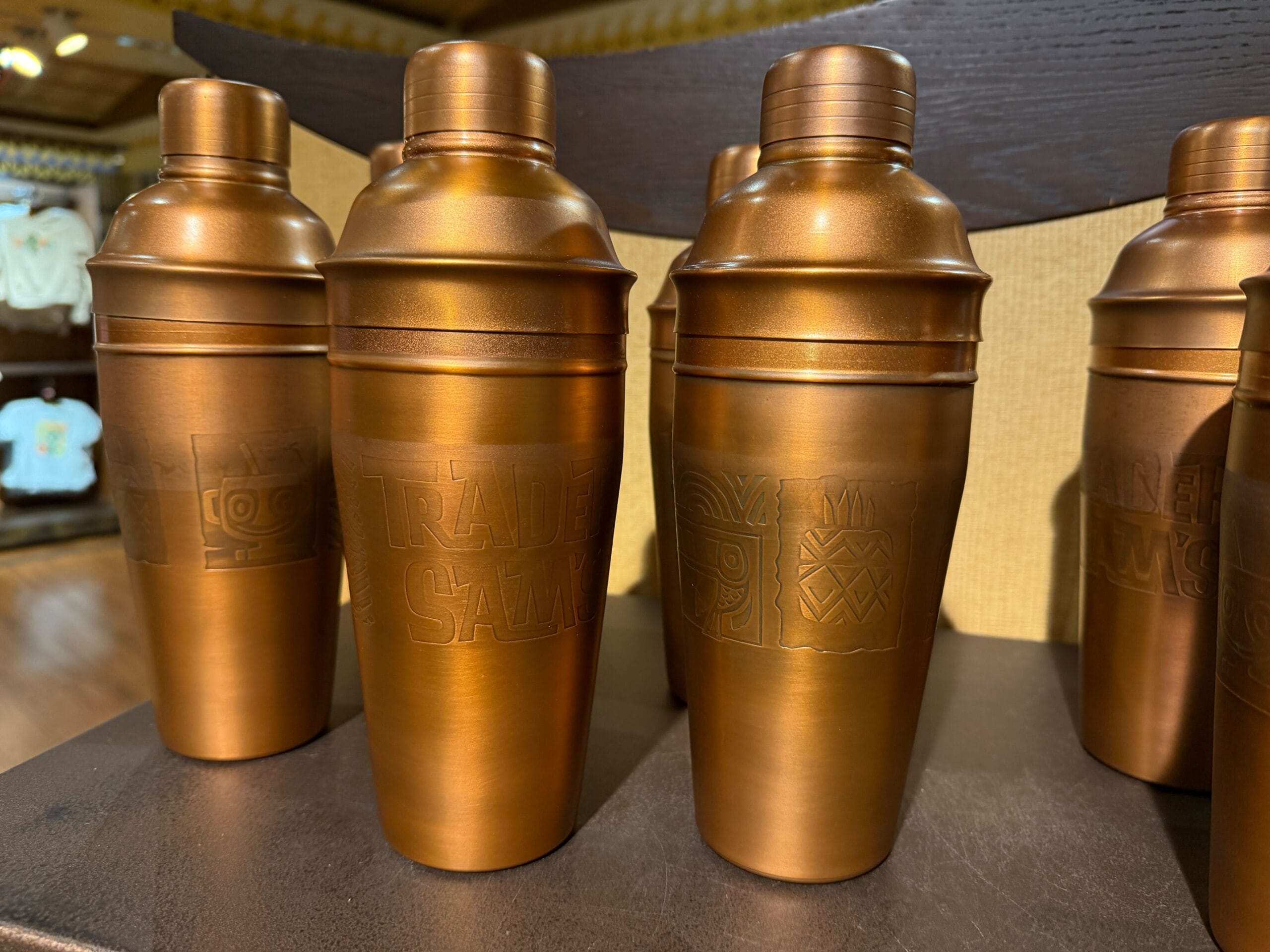 Bronze cocktail shakers with engraved designs inspired by Trader Sam's Shaker, seen on a shop shelf at a Disney Park.