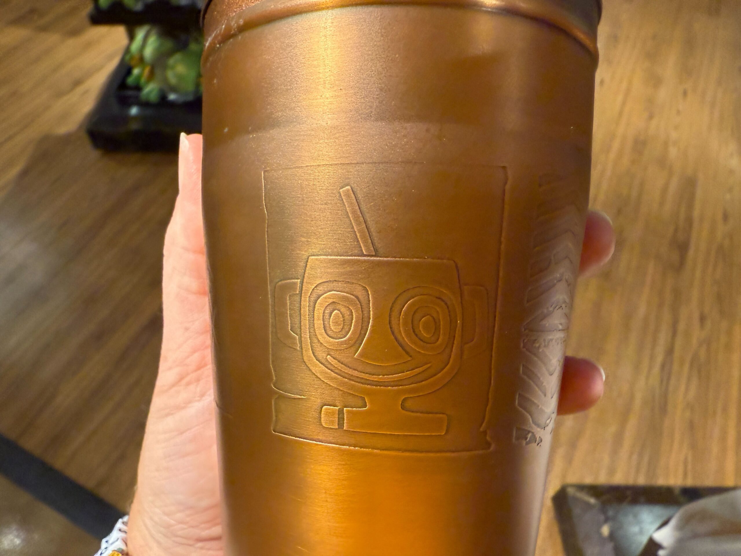 Hand holding a metallic cup featuring an embossed smiling robot—Disney Parks style, ideal for cocktails or Trader Sam's at Disney World.