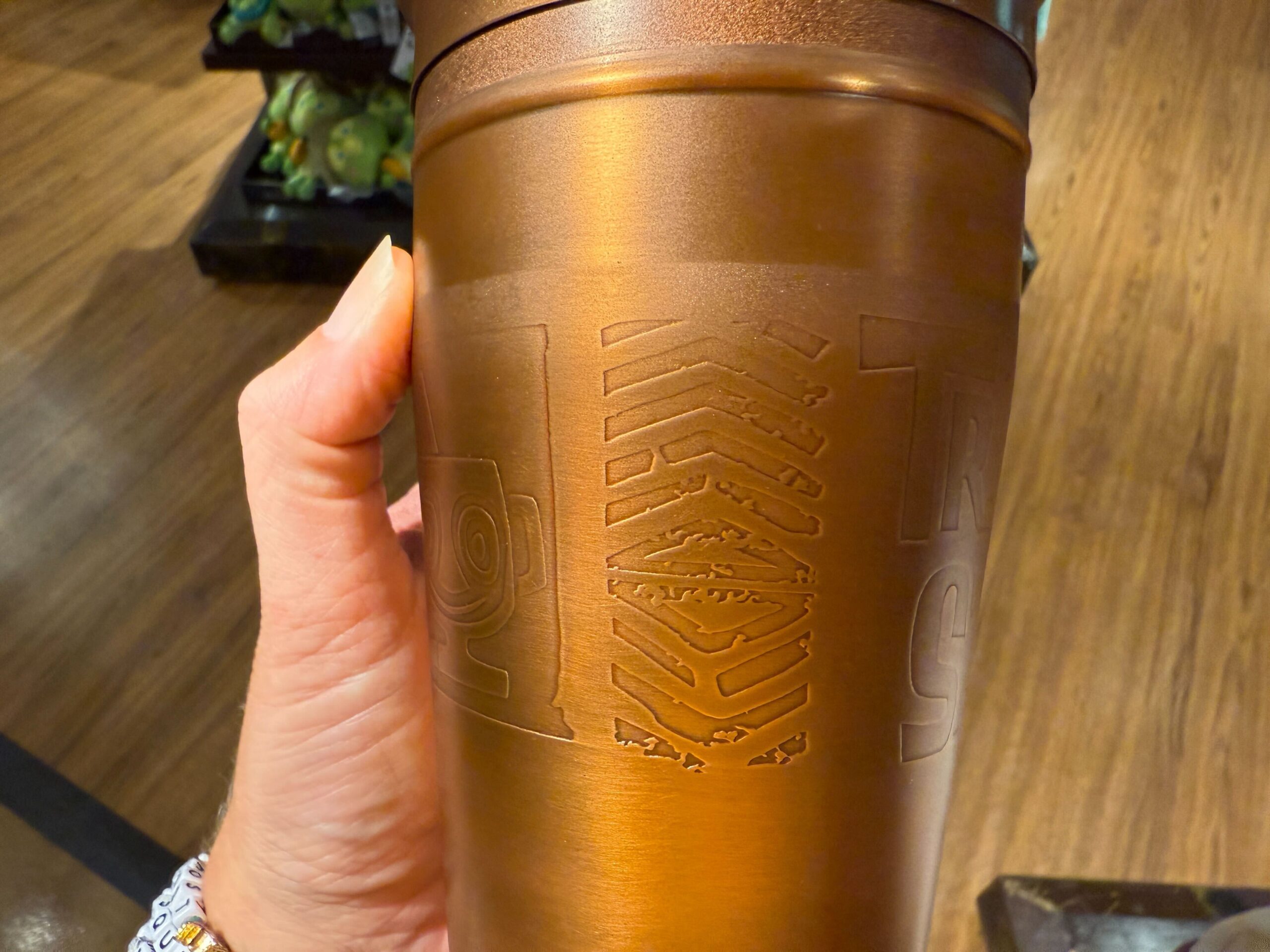 A hand holds a metallic bronze tumbler with a dinosaur fossil, ideal for sipping Trader Sam’s cocktails at Walt Disney World.