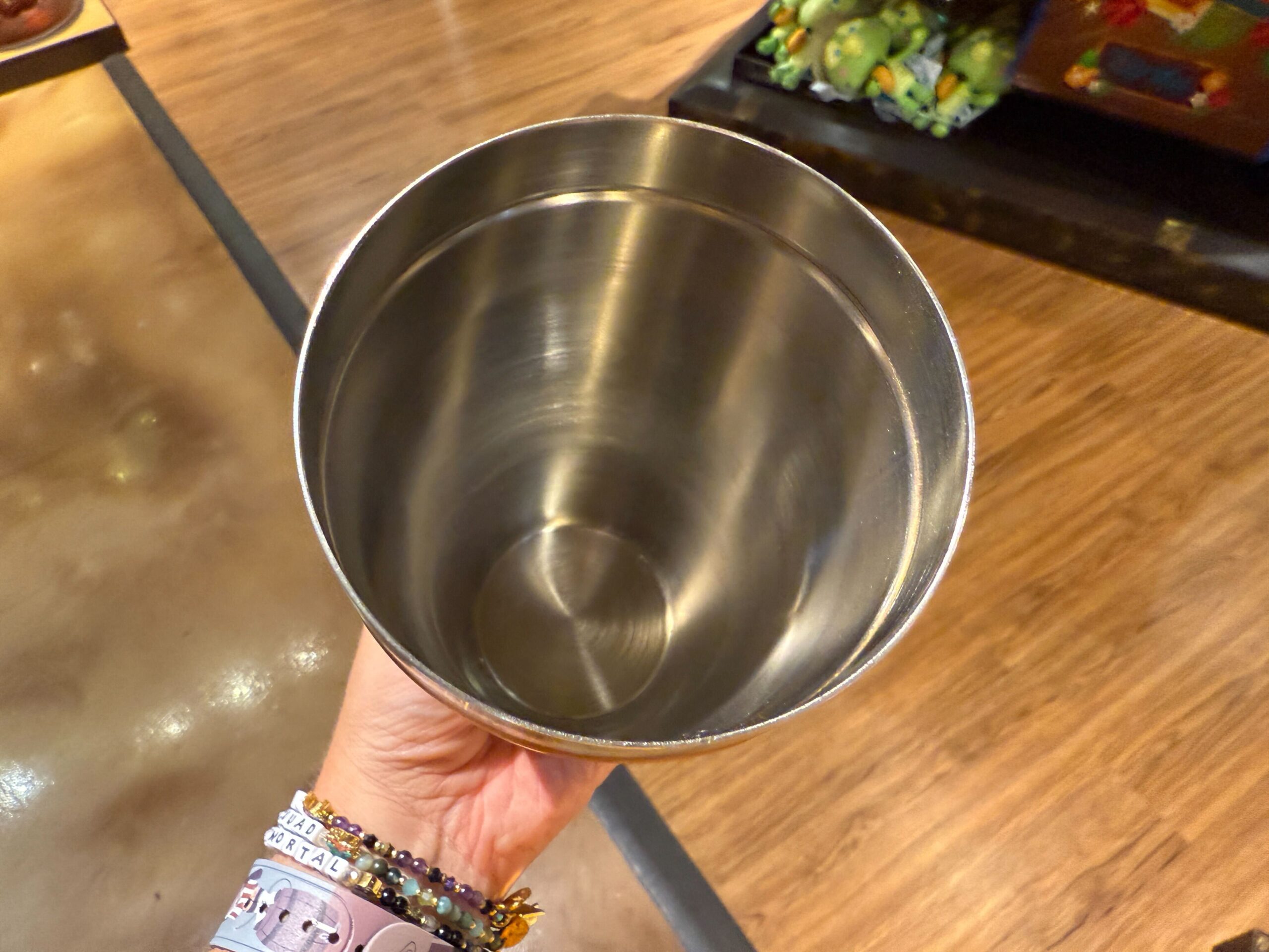 A hand holds an empty stainless steel cocktail cup above a wooden floor, evoking Trader Sam's at Disney World