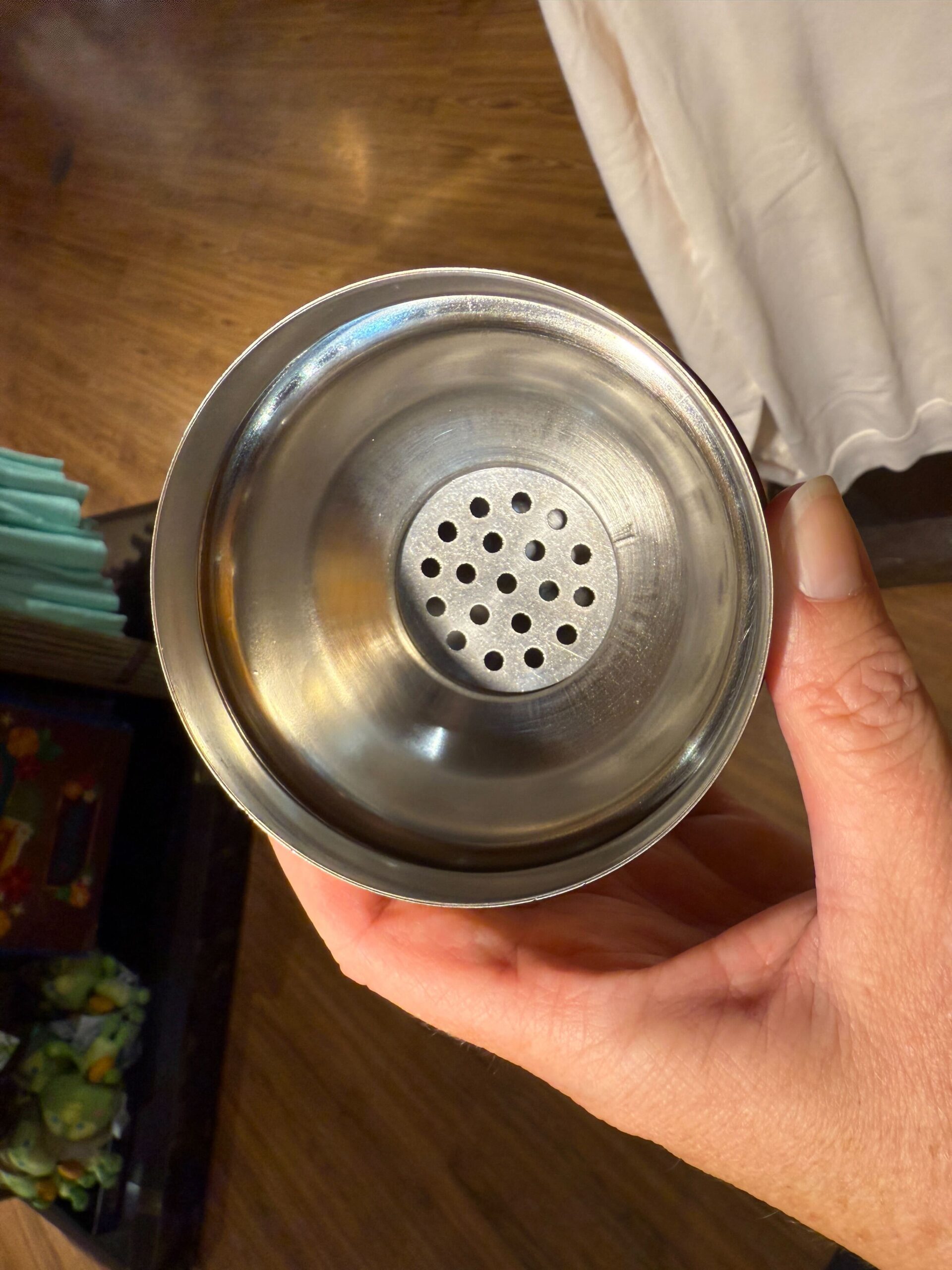 A hand holds a Trader Sam's Shaker metal cup with a perforated strainer