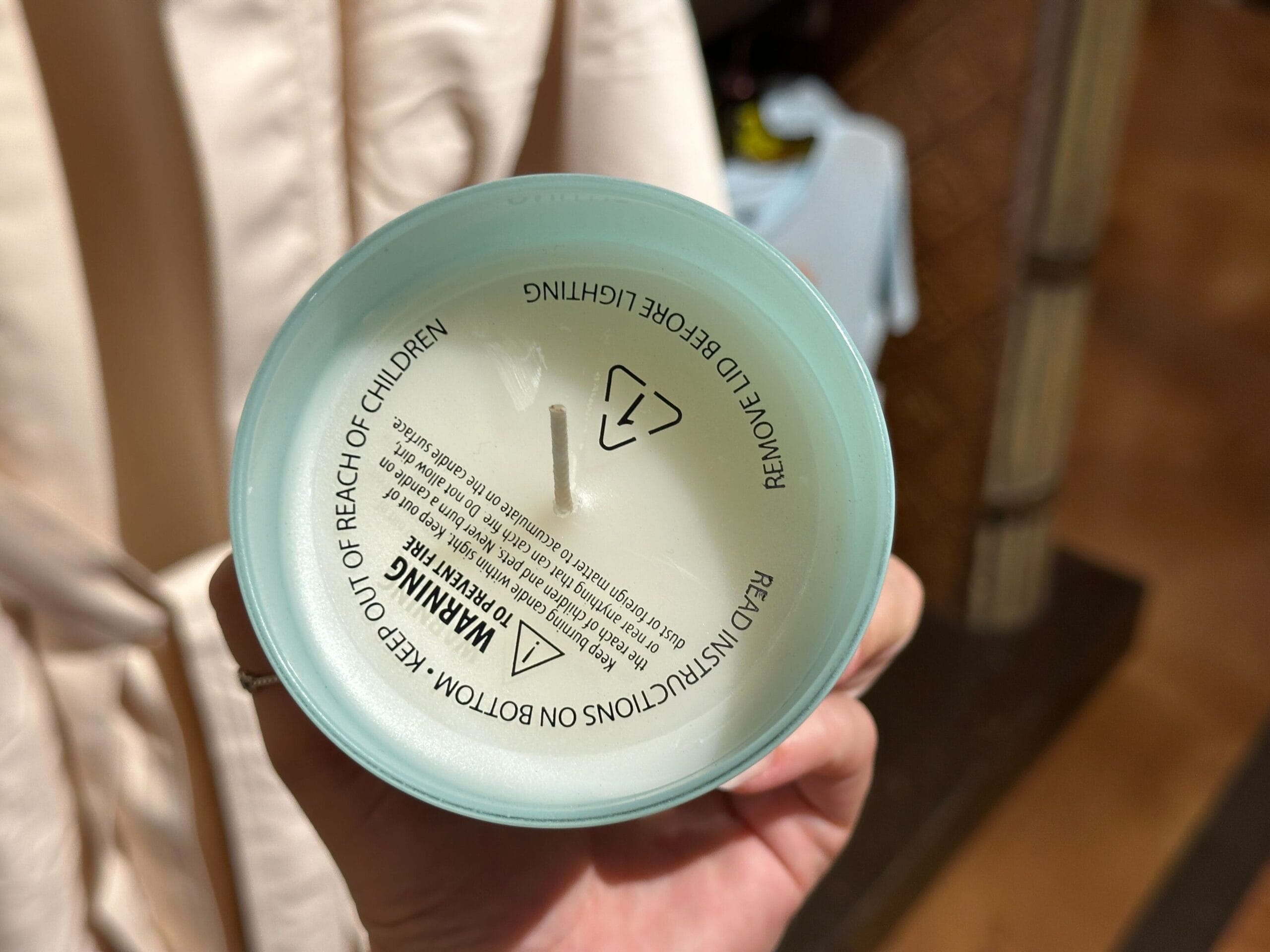 A hand holds a Paradise Candle from above, with two wicks and warning label, styled after Disney’s Polynesian Village Resort.