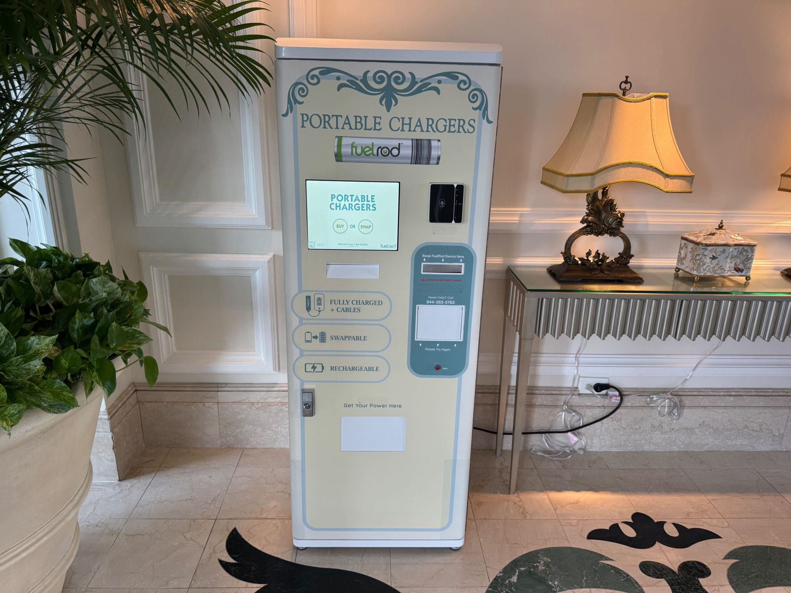 A FuelRod portable charger vending machine sits in a themed Disney hallway adorned with greenery and whimsical lamplight.