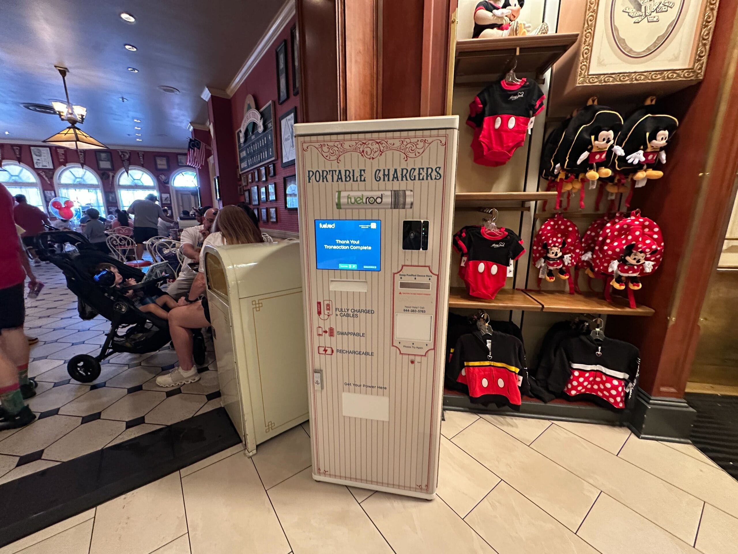 A FuelRod Kiosk vending machine sits in a Disney park shop, surrounded by Minnie Mouse outfits similar to those found at Disneyland.