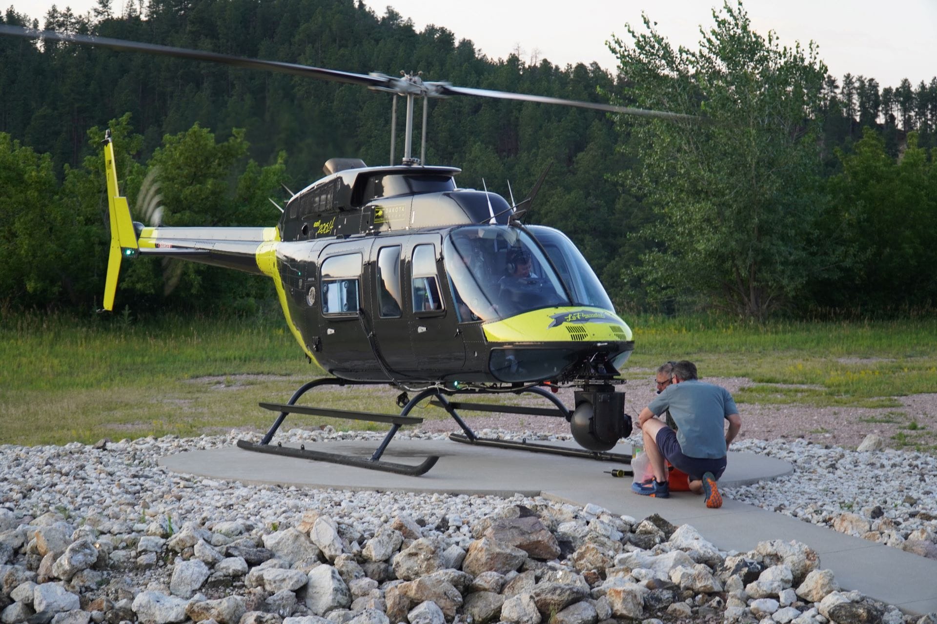 Behind-the-scenes at Disney: Two people kneel by a yellow and black helicopter on a rocky helipad for Soarin' Across America
