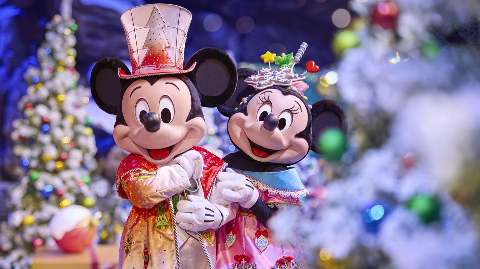 Mickey and Minnie Mouse in festive costumes smile by Christmas trees at Disneyland Paris, near the castle distinct from Magic Kingdom’s.