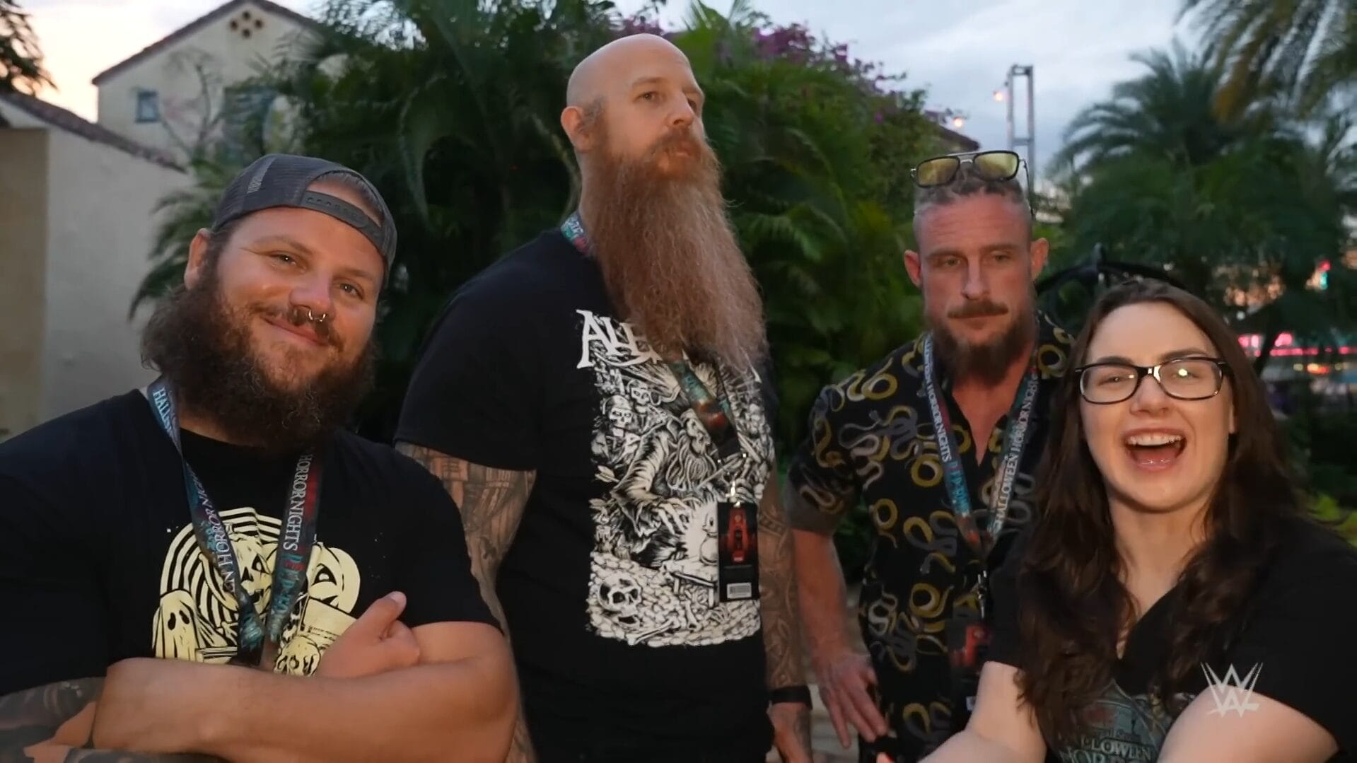 Four friends smile outdoors with lush greenery behind them, excited for Disney park Halloween festivities and castle spotting.