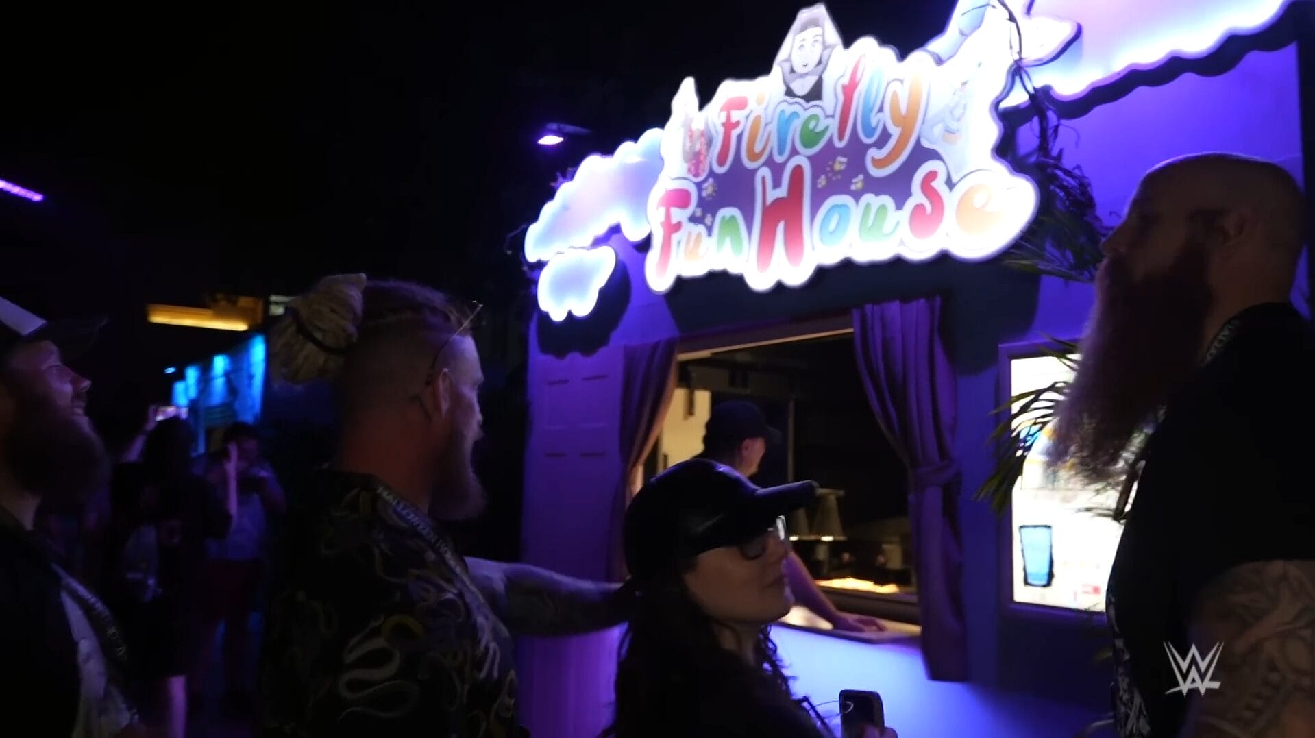 Three stand by neon "Firefly Fun House" at Halloween Horror Nights, Wyatt Sicks glowing behind—no castle like those in Disney Parks.