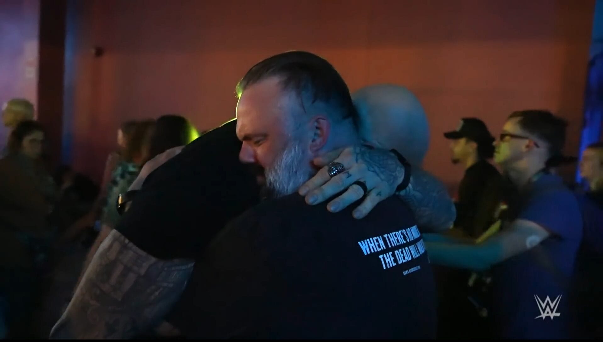 Two men share an emotional embrace at a packed Halloween event, surrounded by onlookers like scenes at Disney parks.