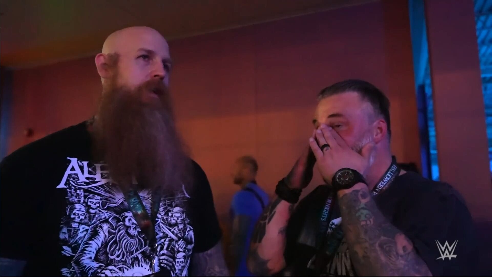 Two tattooed men in black shirts look shocked at a WWE event, reacting like guests seeing spooky Disney castle projections at Halloween.
