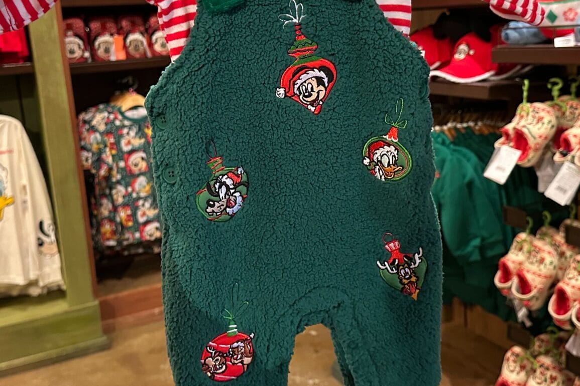 سرهمی پشمالوی سبز نوزادی با چهره شخصیت‌های دیزنی به شکل گوی‌های تزئینی کریسمس، در ویترین فروشگاهی که یادآور پارک‌های دیزنی در تعطیلات است.