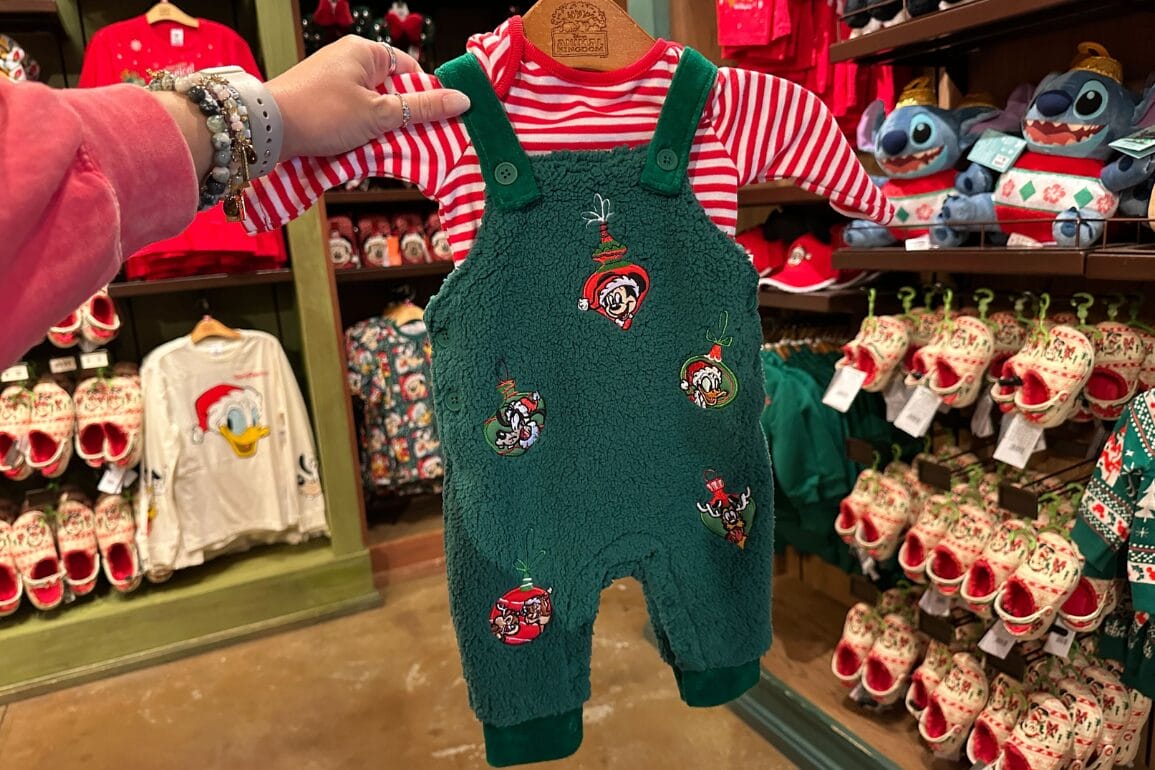 سرهمی نوزادی پشمالوی سبز دیزنی با تکه‌دوزی شخصیت‌ها و آستین‌های راه‌راه قرمز که در یک فروشگاه تعطیلات در پارک دیزنی نگه داشته شده است.