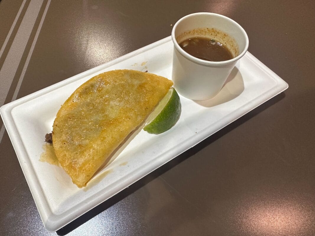 A quesabirria taco served with a lime wedge and consommé, featured at Walt Disney World Jollywood Nights 2025. No castle shown.