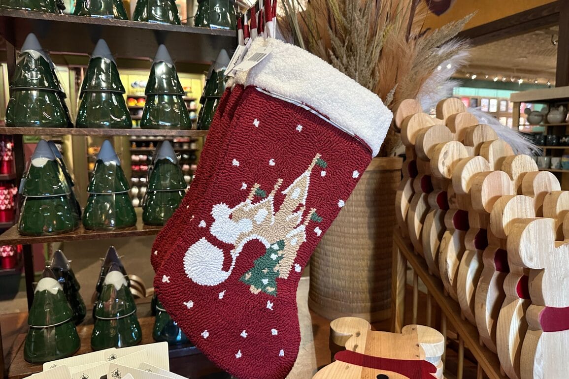 یک جوراب کریسمس قرمز با طرحی شبیه به کوتوله در میان تزئینات جشن در یک فروشگاه آویزان است، یادآور ویترین‌های تعطیلات در پارک‌های دیزنی.