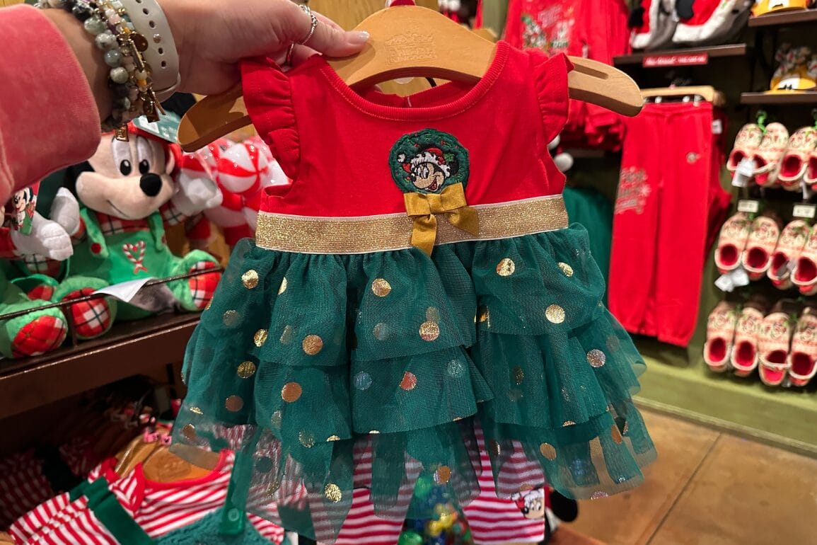 لباس نوزادی شاد قرمز و سبز با نقطه‌های طلایی، حلقه گل مینی ماوس، ایده‌آل برای پوشیدن در تعطیلات پارک‌های دیزنی، در فروشگاه به نمایش گذاشته شده است.