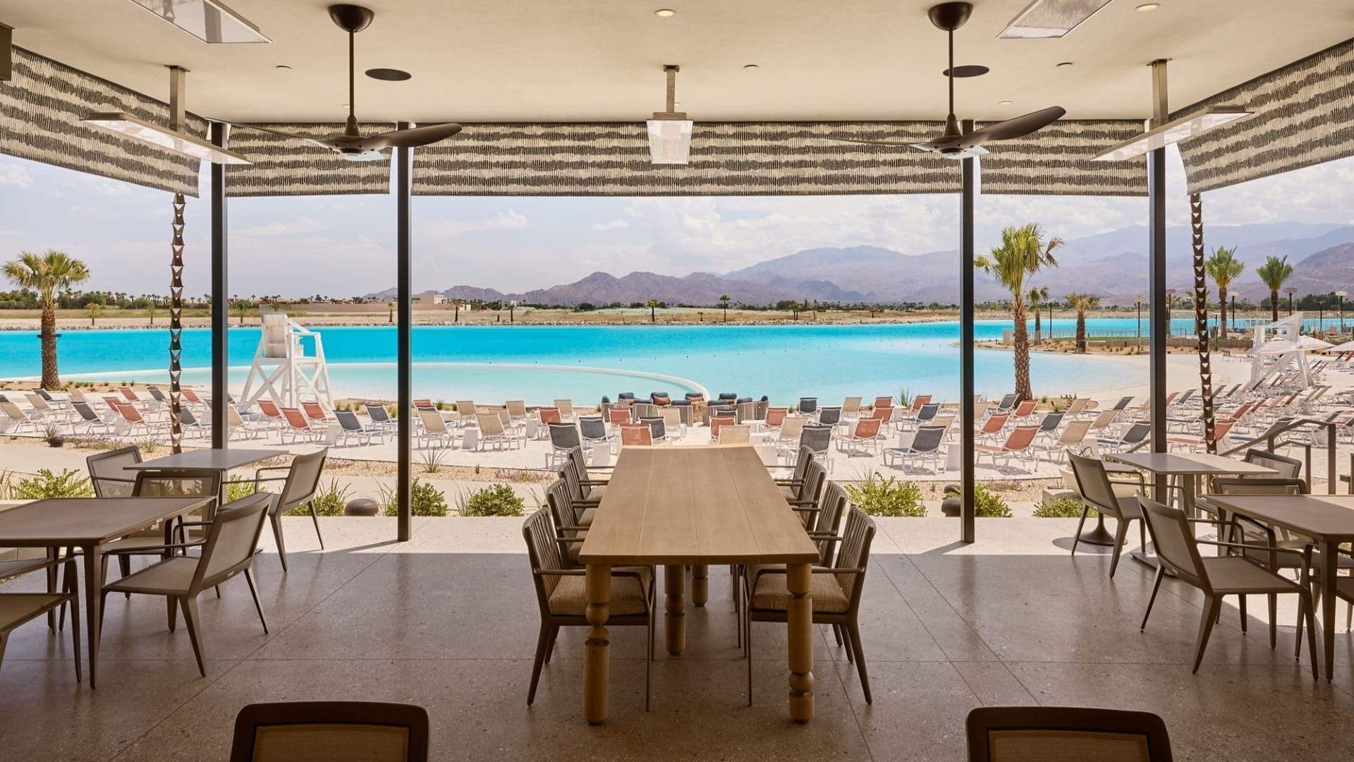 Shaded patio with tables and chairs, overlooking a pool, palm trees, and mountains—evokes a Disney resort atmosphere.