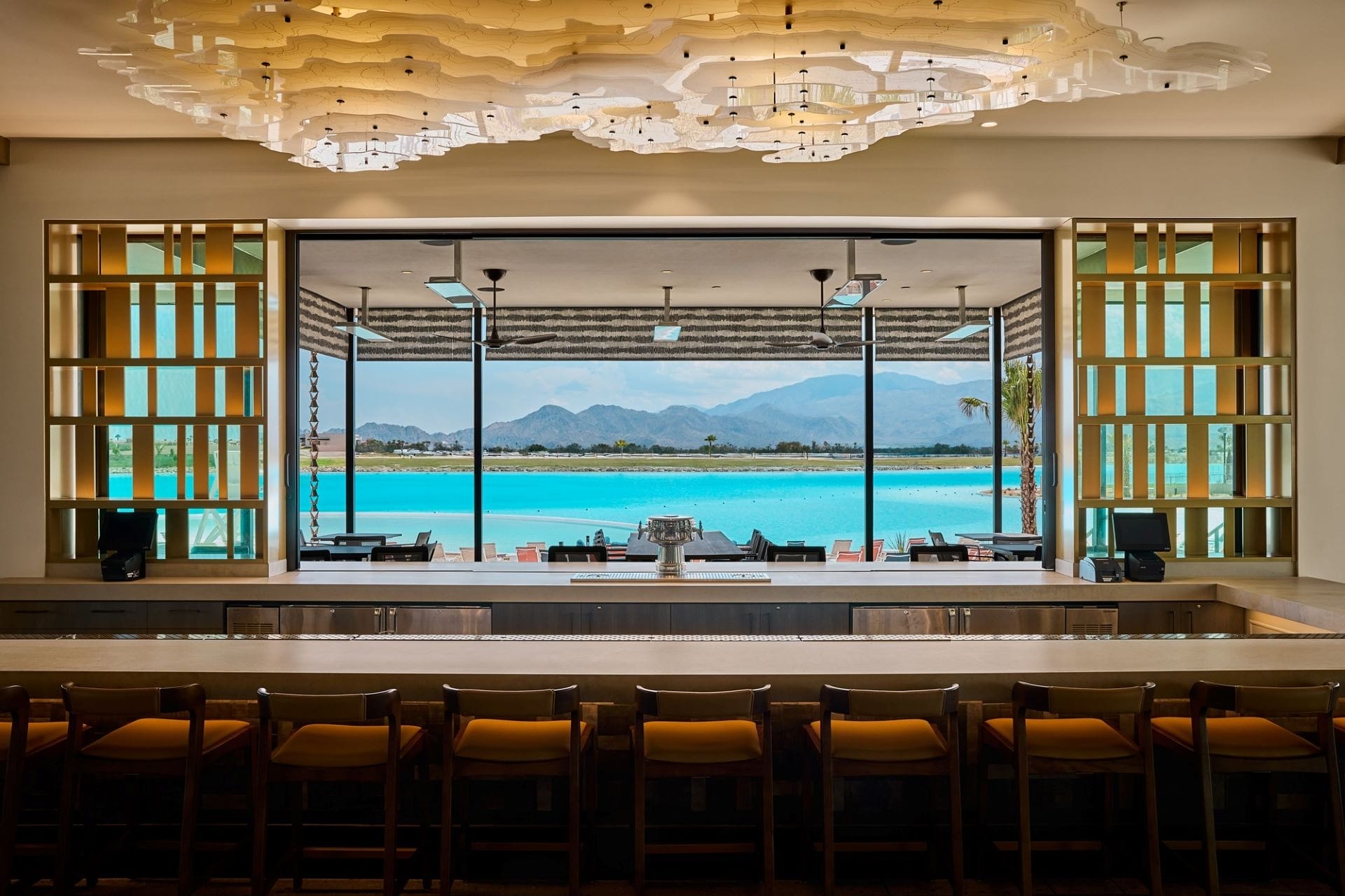 A sleek bar with turquoise water, palm trees, and mountains outside large windows, reminiscent of Disney resort lounges worldwide.