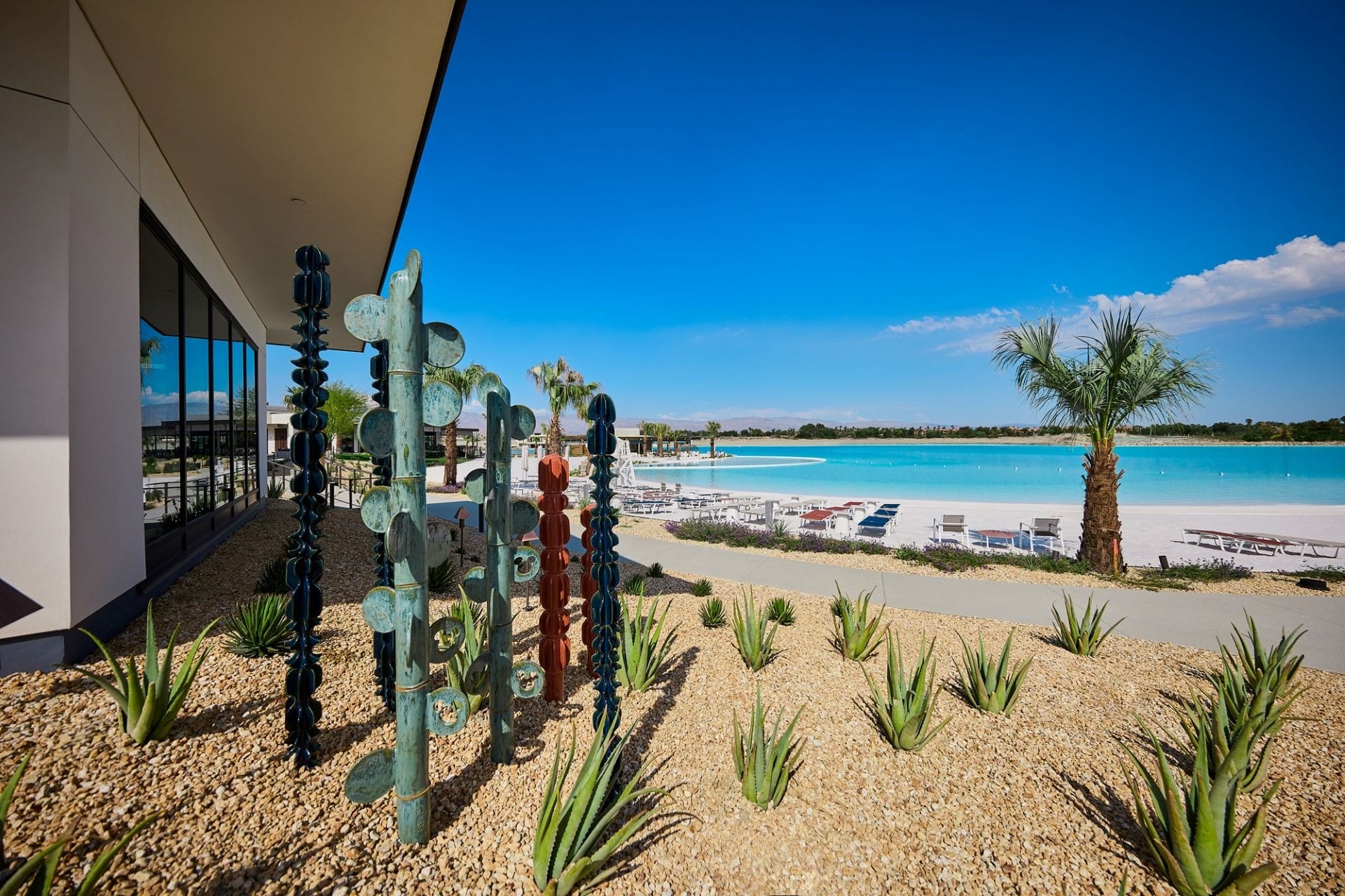 Modern metal sculptures and desert plants outside a building near a large blue pool and palm trees, reminiscent of Epcot’s landscaping.