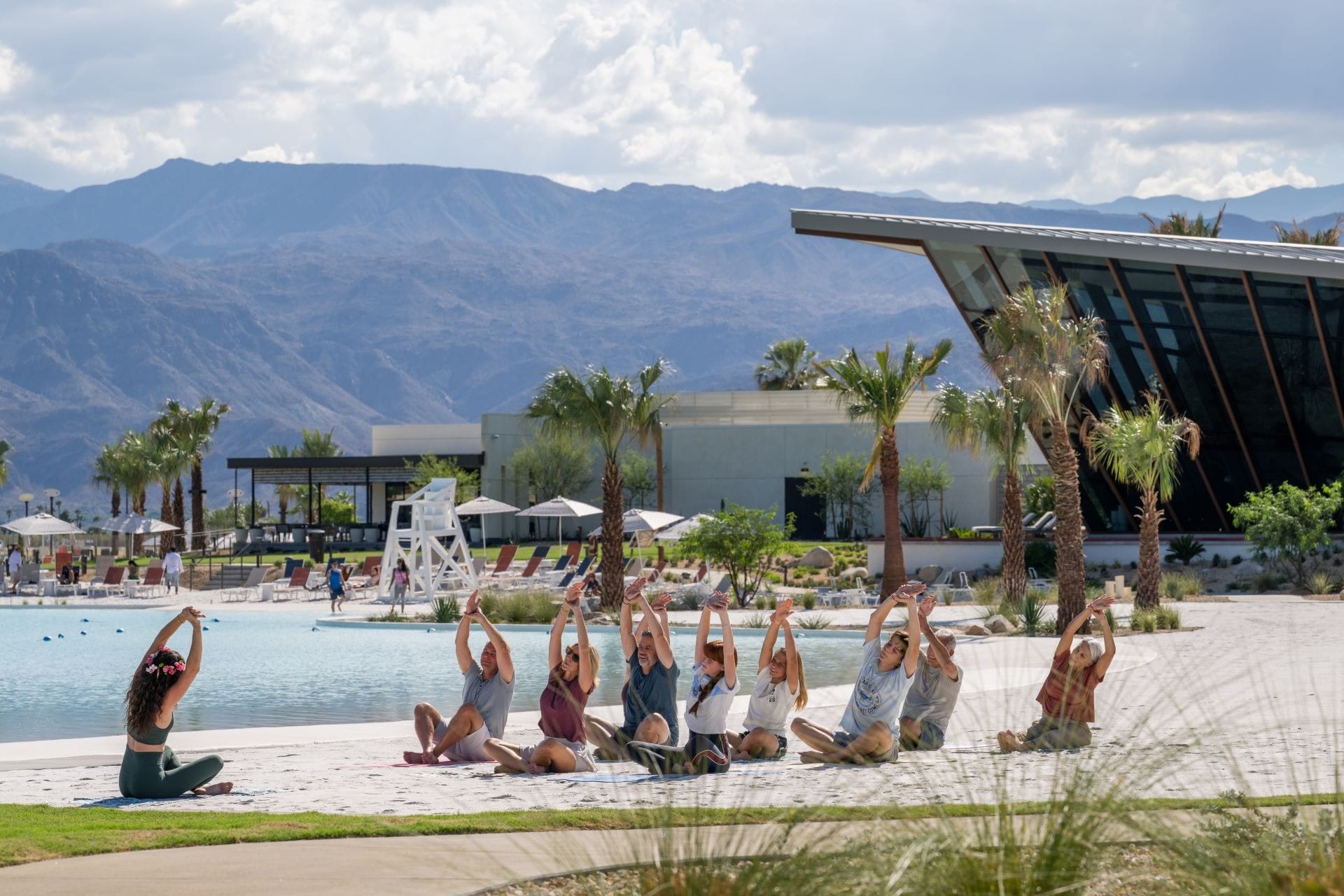 A group practices yoga by a pool at Cotino, a Storyliving Community, with scenic mountains and modern buildings, no castle in sight.