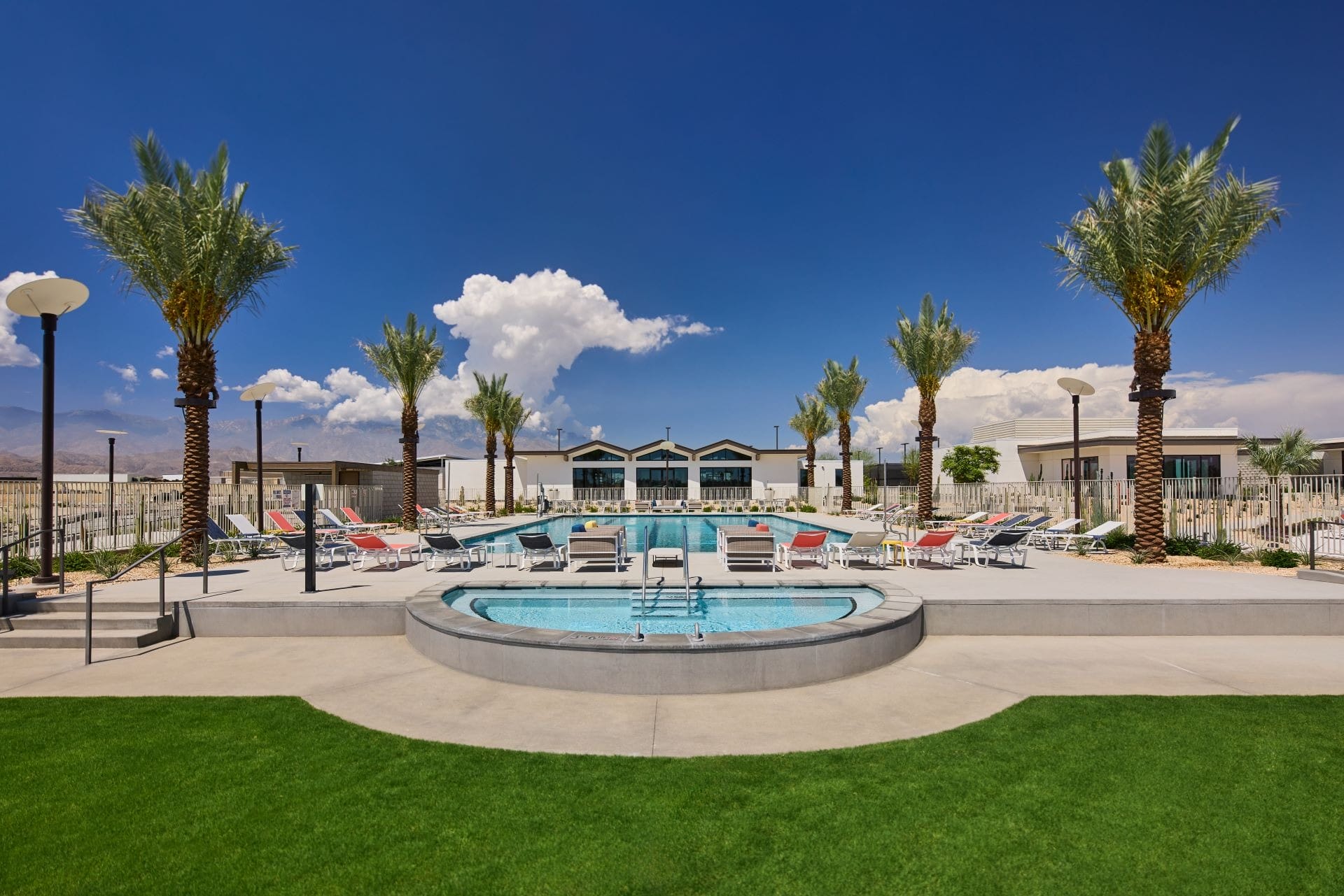 A small circular pool with lounge chairs and palm trees, reminiscent of a Disney resort, set beneath a blue sky with clouds.