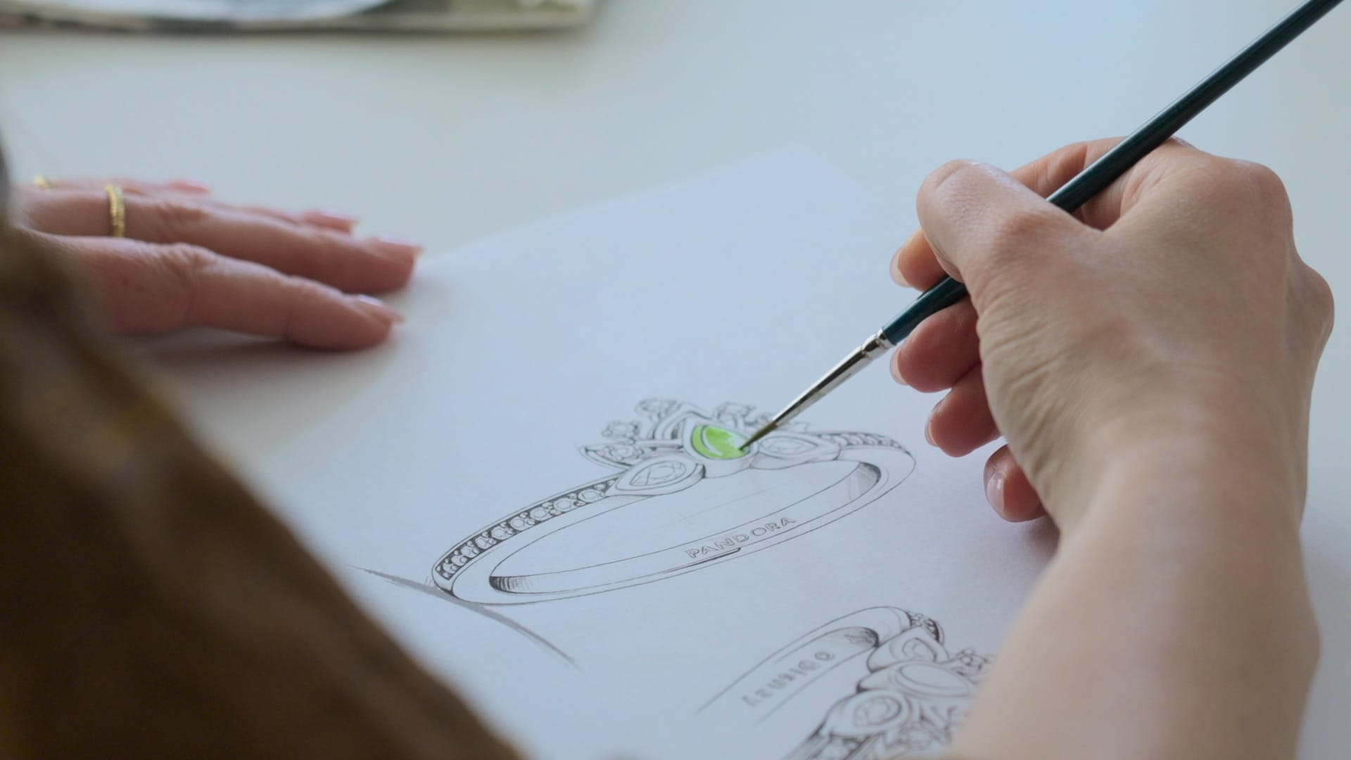 Someone paints green onto a Disney Princess Pandora ring sketch, echoing the artistic spirit found throughout Disney parks worldwide.