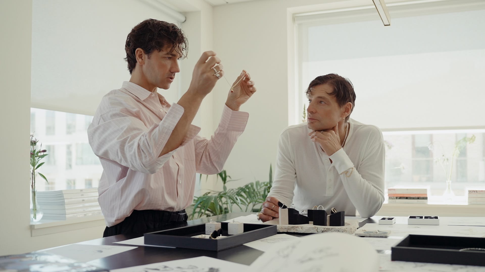 Two men review Pandora jewelry at a sunlit table, with sketches and trays, similar to creative sessions near Disney park castles.