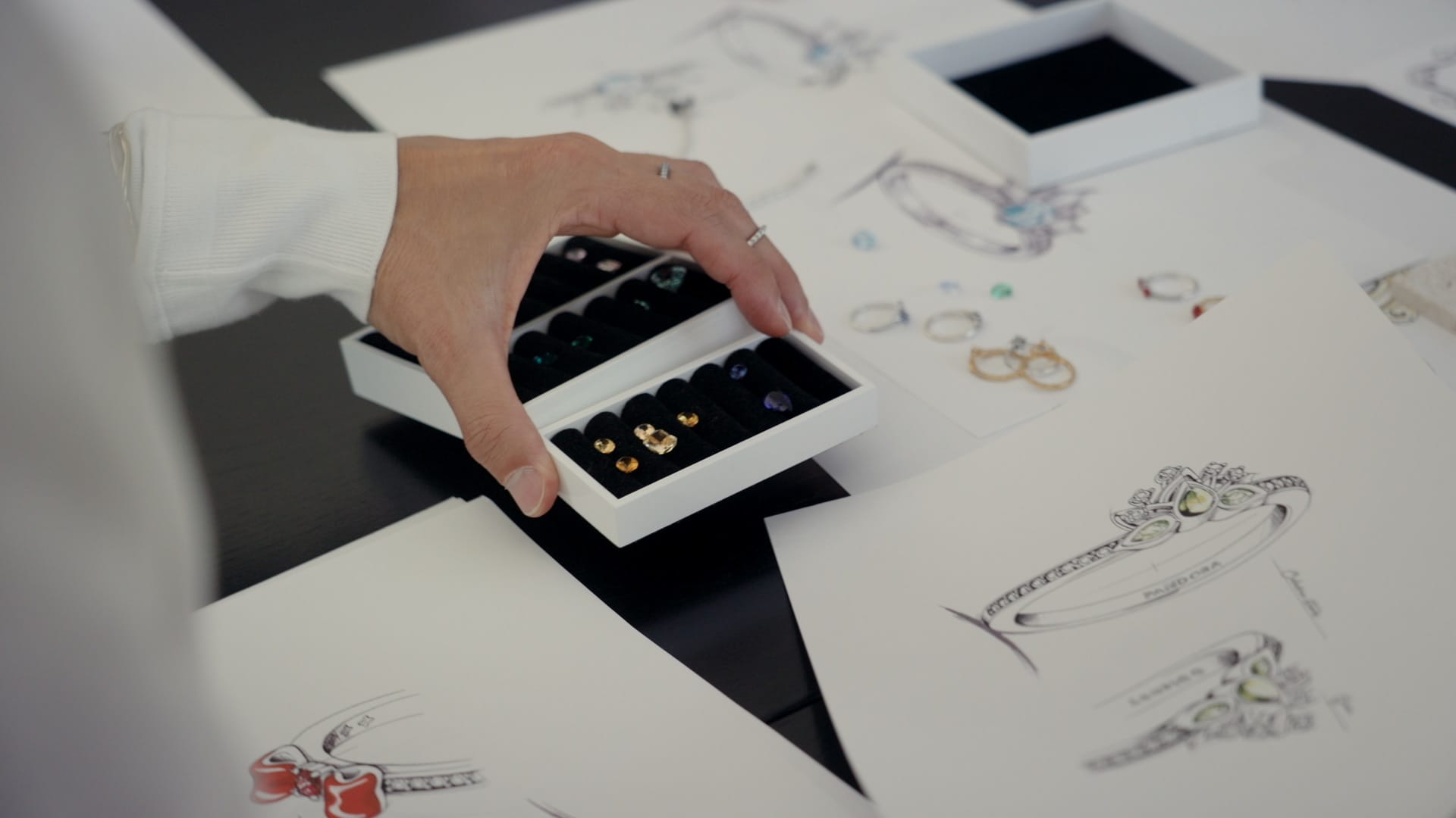 A hand holds a Pandora jewelry box with gemstones above ring sketches and Disney Princess rings, evoking the magic of Disney parks.