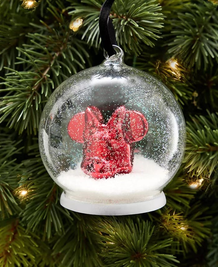 Holiday 2025 clear ornament with red Mickey ears and fake snow, hanging on a lit Disney park tree sparkling with lights.