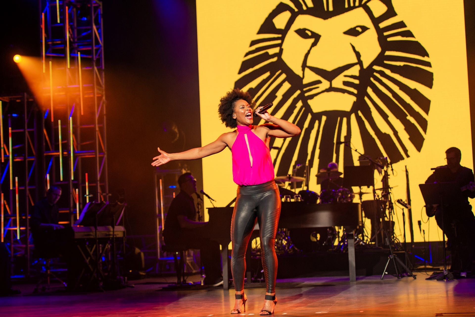 Woman sings at EPCOT Festival of the Arts 2026 with Lion King logo and band behind her, no castle in sight at this Walt Disney park.