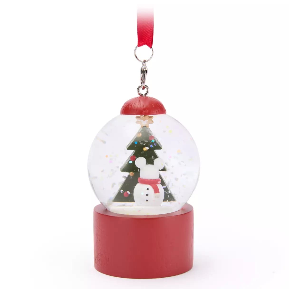 A snow globe ornament with a snowman and Christmas tree inside, hanging from a red ribbon, on a red base.
