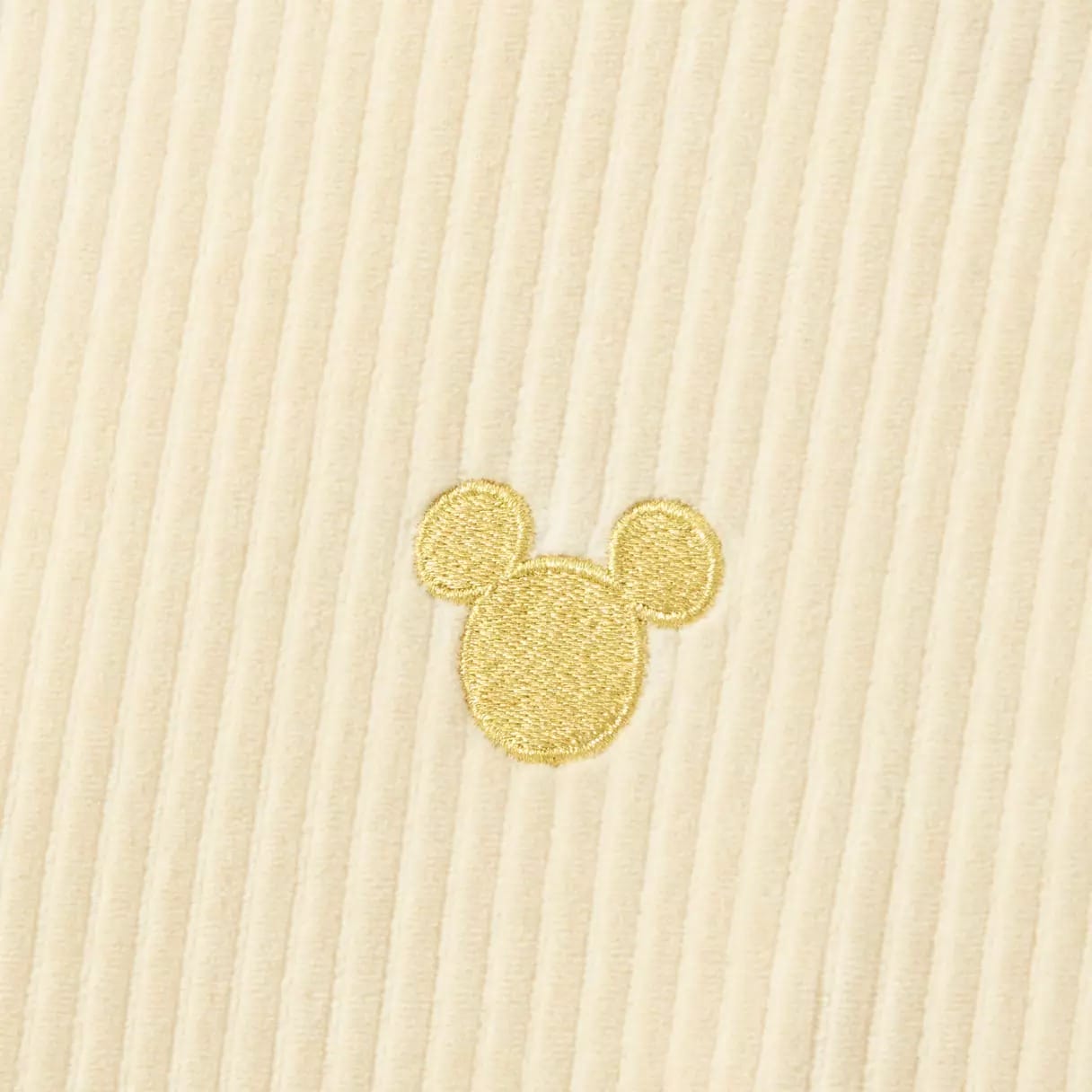 Beige corduroy fabric with a small, gold embroidered silhouette of a mouse head with two round ears.