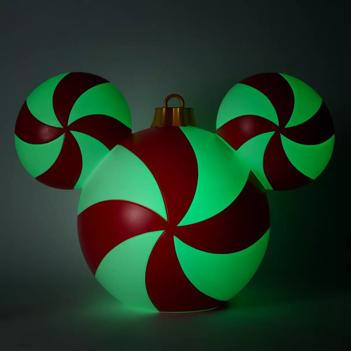 Glowing ornament shaped like Mickey Mouse with red and green peppermint swirl patterns on a dark background.