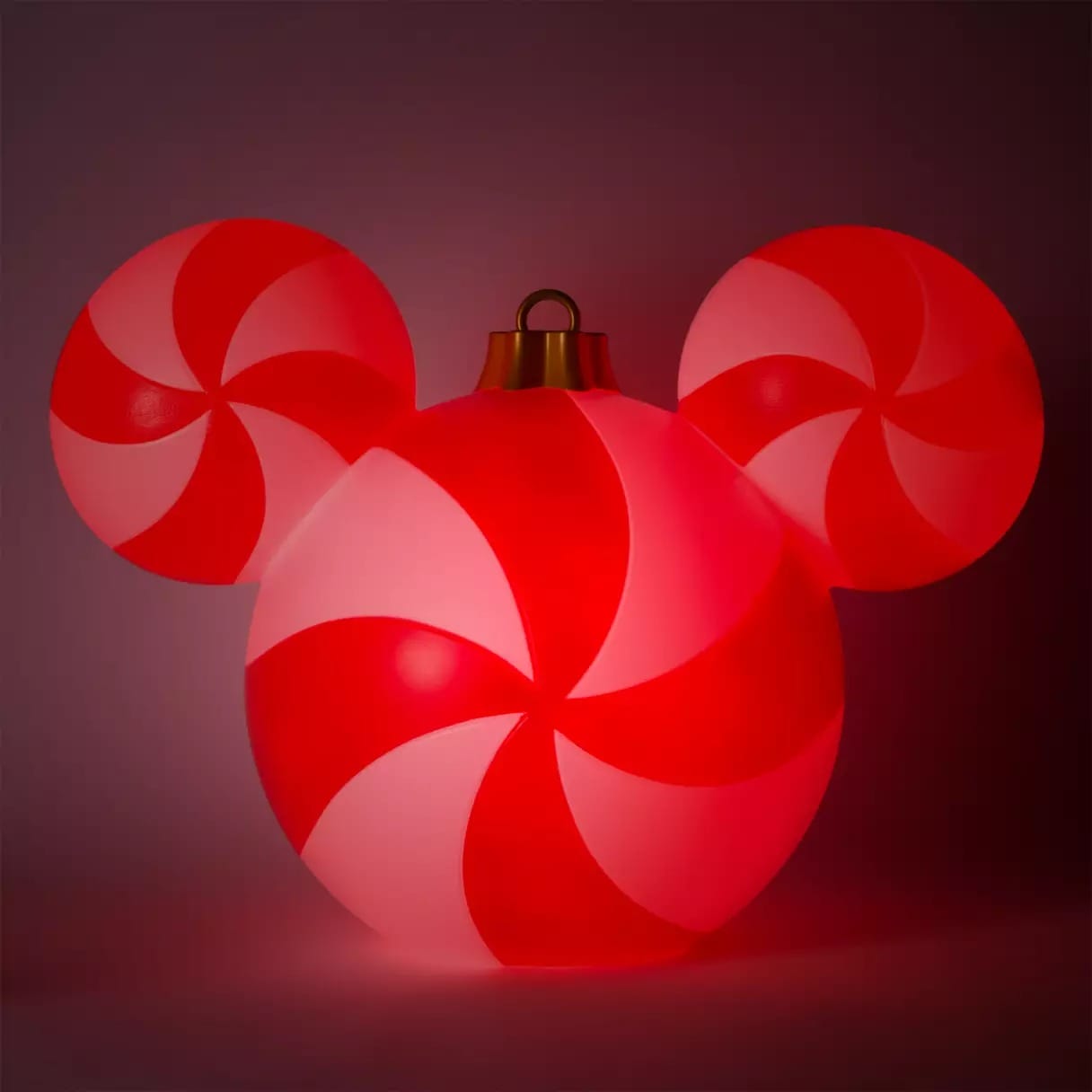 A glowing red and white ornament shaped like Mickey Mouse, with a peppermint swirl pattern on each circle.