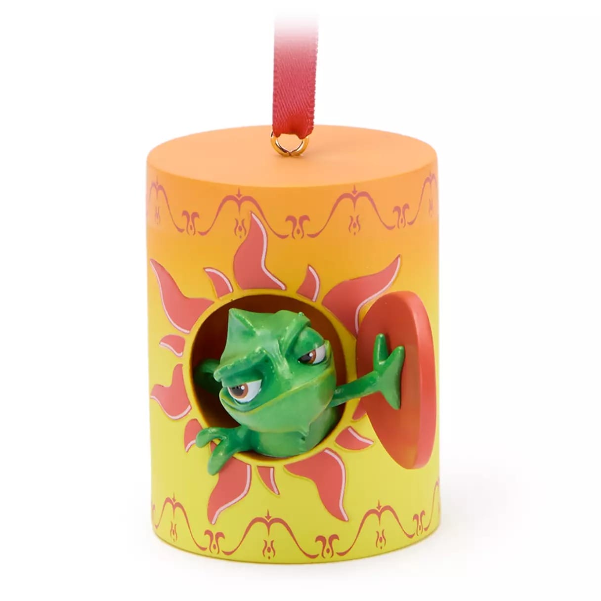 A green chameleon figurine peeks out of a sun-patterned yellow ornament with a red ribbon hanger.